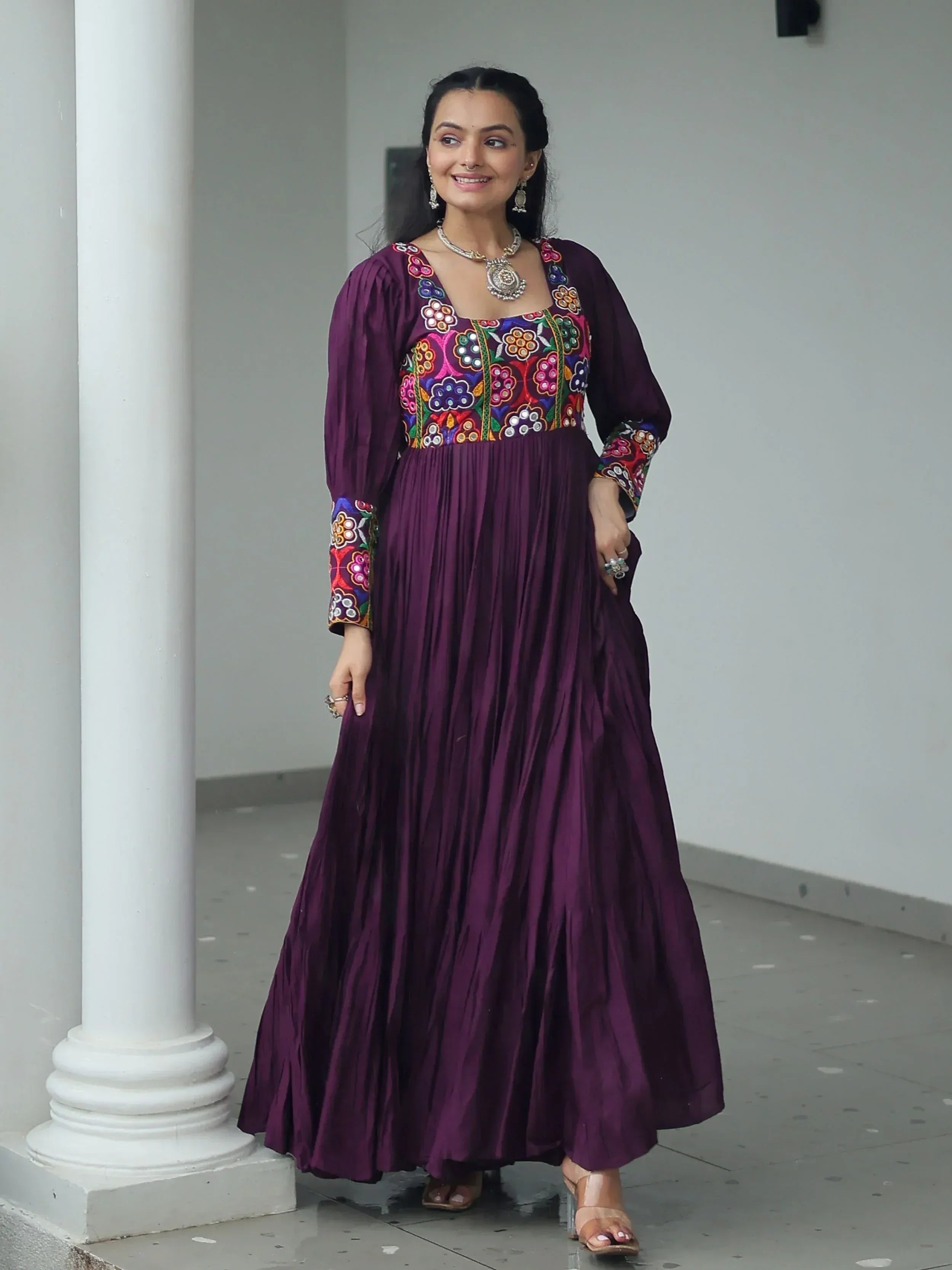 Purple ethnic gown with colorful floral embroidery, pleated skirt, and traditional jewelry for women