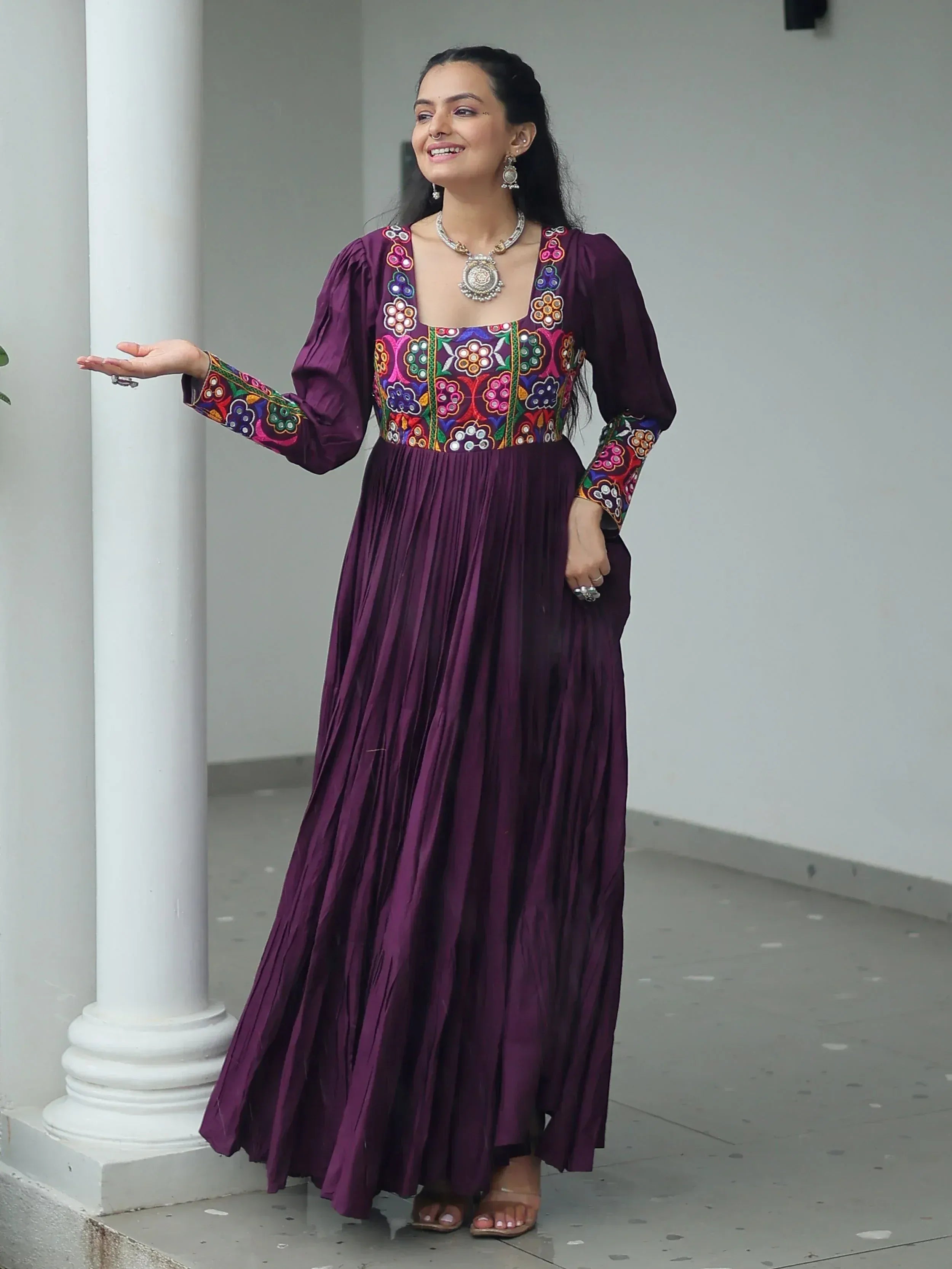 Purple ethnic gown with colorful floral embroidery, pleated skirt, and traditional jewelry for Indian wear