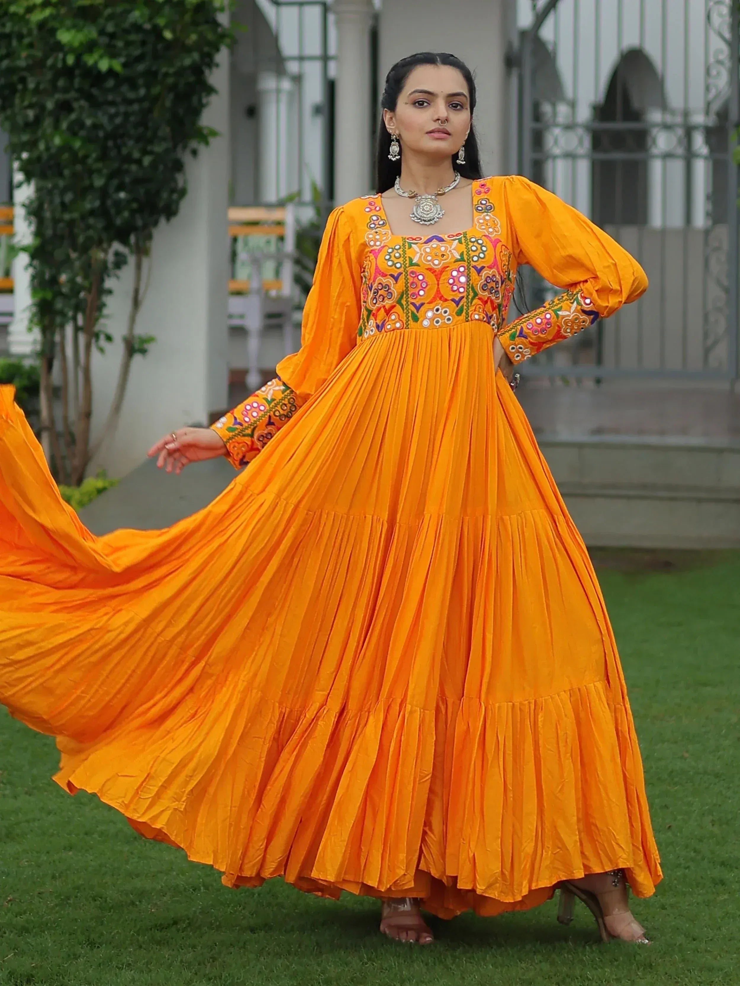 Vibrant orange ethnic gown with floral embroidery, pleated skirt, and puff sleeves for festive occasions.