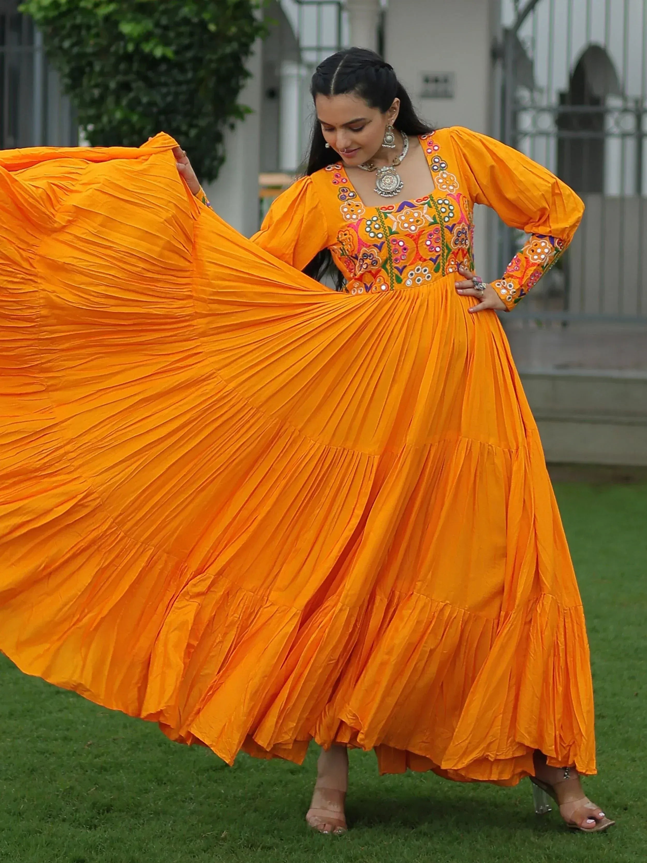 Vibrant orange ethnic gown with floral embroidery and pleated skirt, perfect for Indian festive wear.