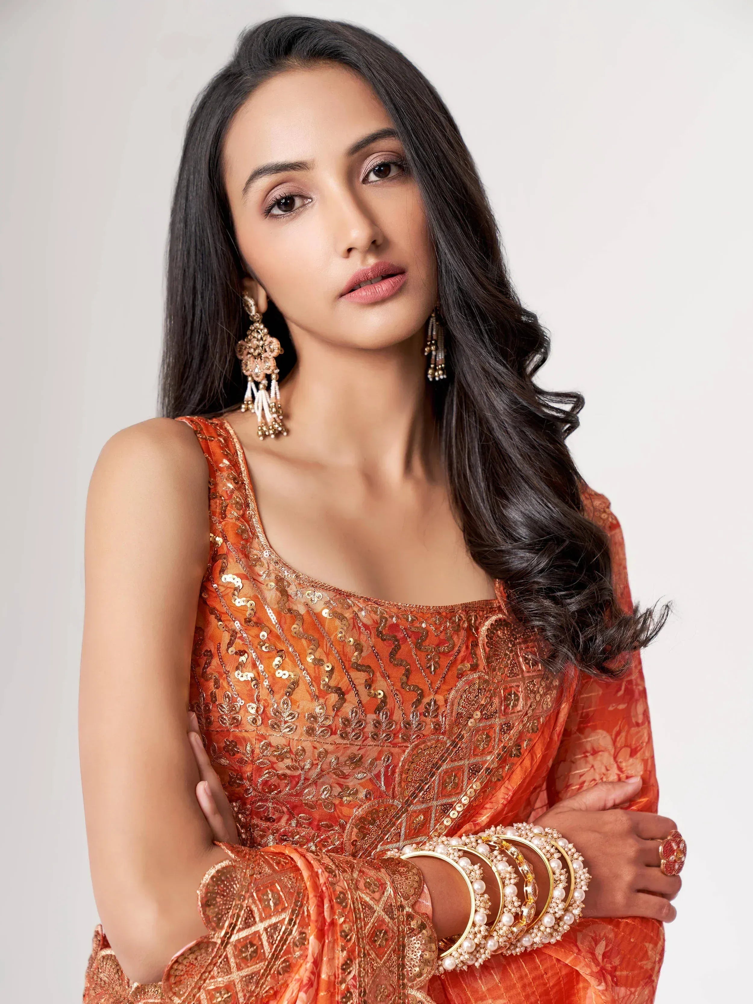 Woman in orange sequined ethnic gown with gold embroidery, statement earrings, and pearl bangles