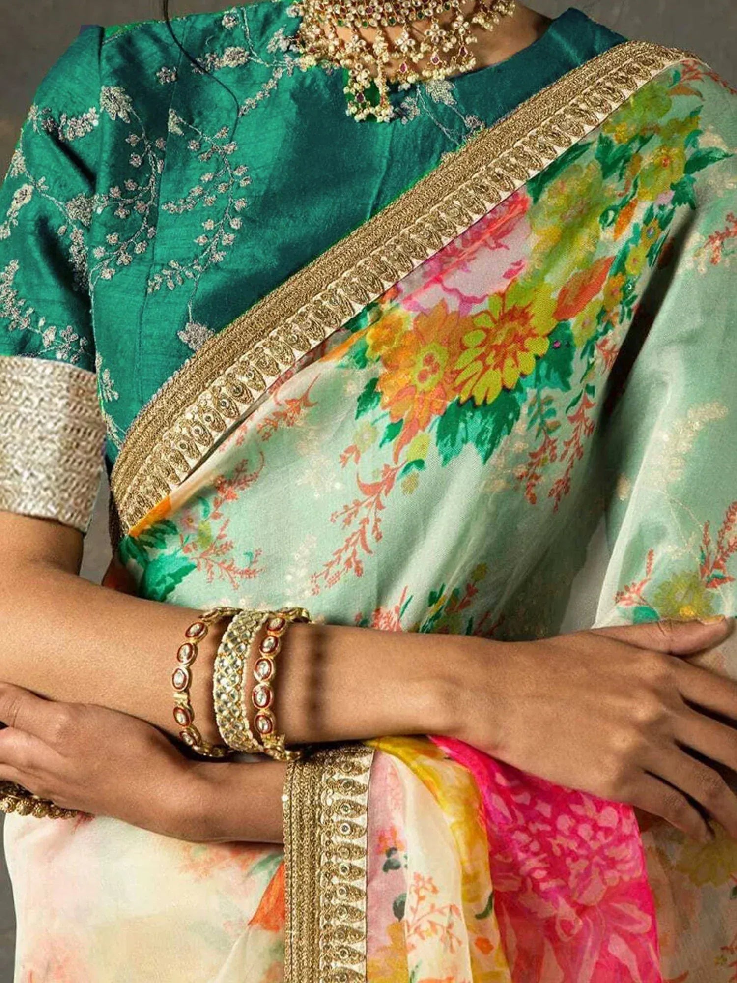 Emerald green embroidered blouse with floral print saree, gold border, and traditional jewelry