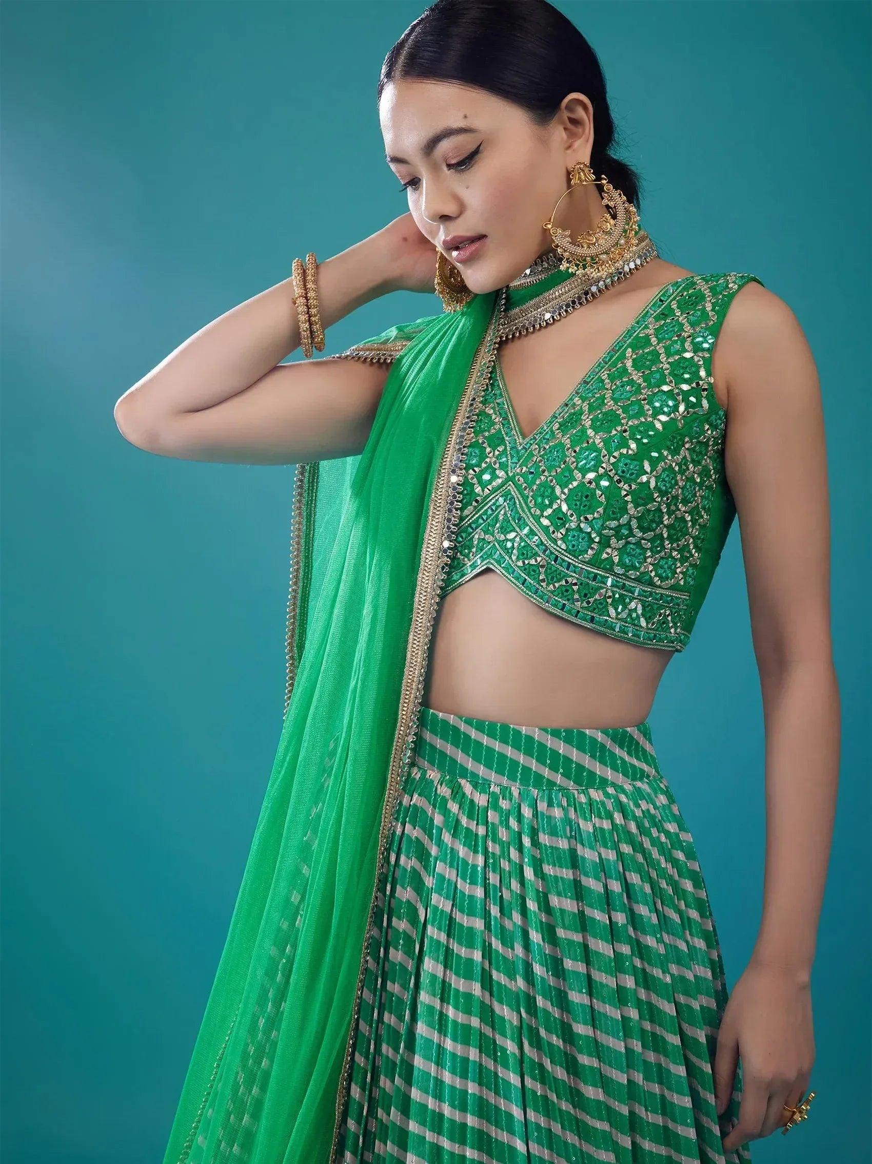 Emerald green embroidered lehenga choli with striped skirt and gold jewelry, perfect for Indian ethnic wear