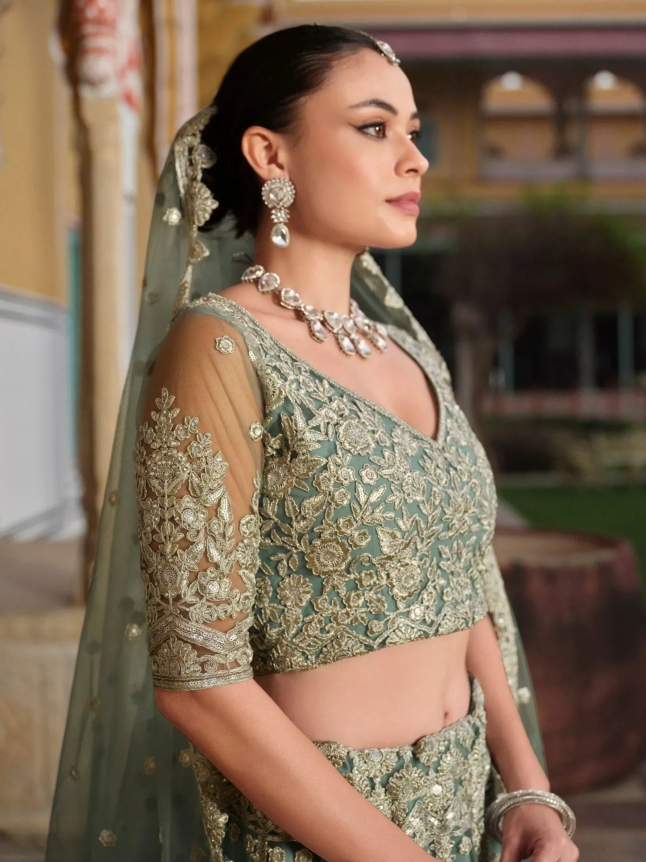 Elegant sage green lehenga choli with gold floral embroidery, sheer sleeves, and matching dupatta for Indian weddings
