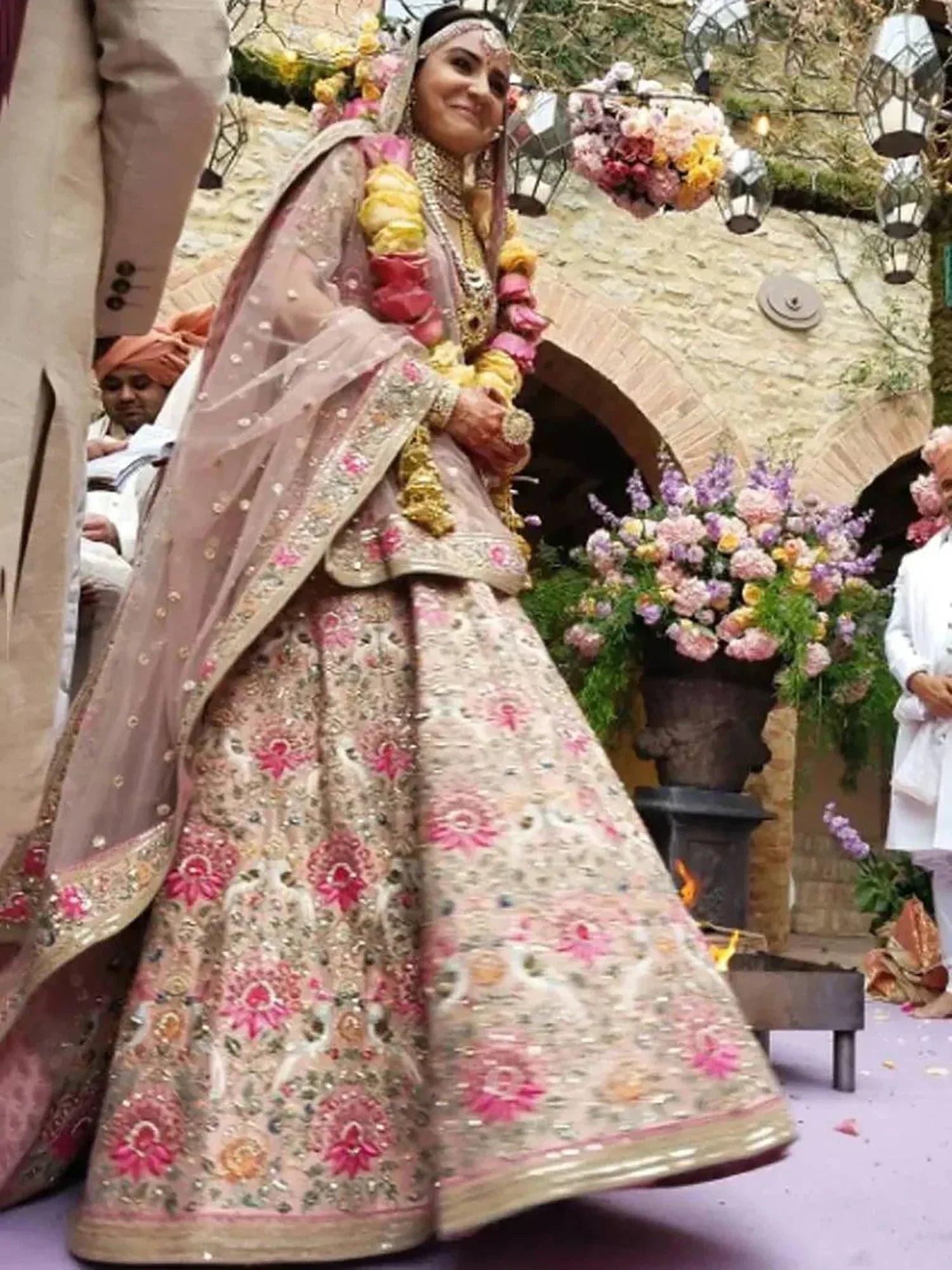 Bride in pink floral embroidered lehenga choli at Indian wedding ceremony with floral decor