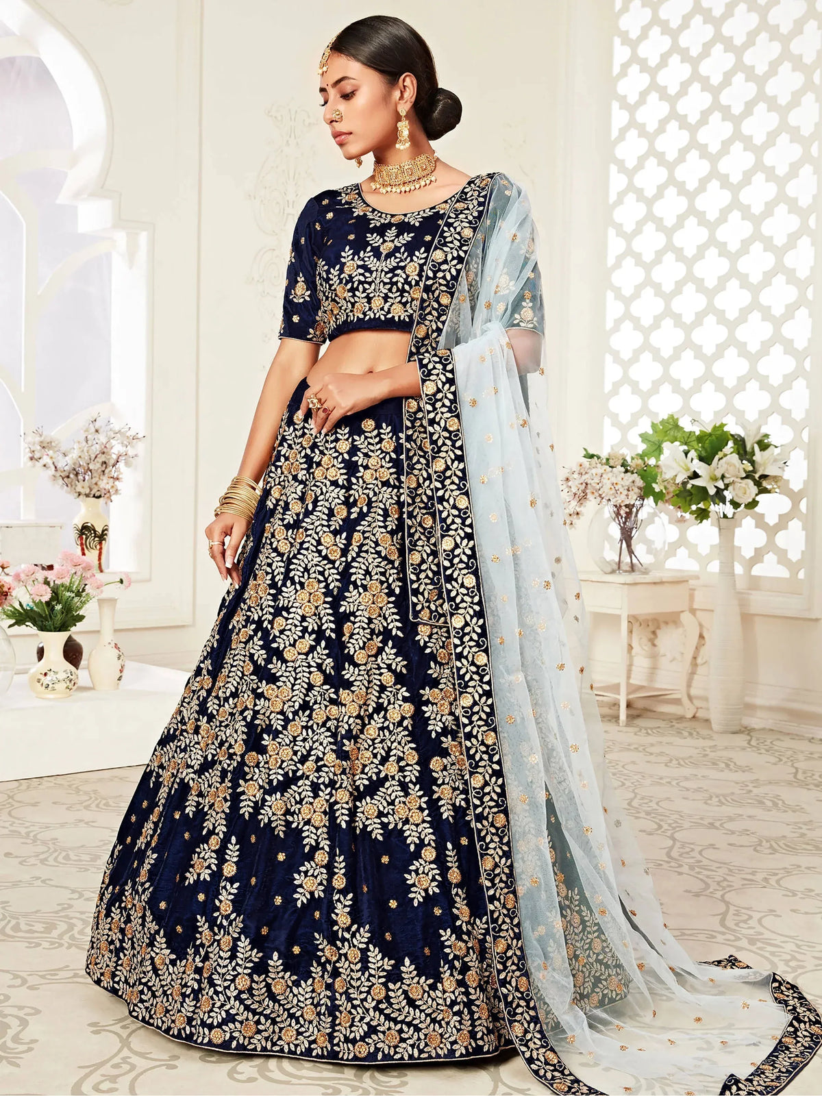 Woman wearing a navy blue velvet lehenga choli with gold embroidery and a light blue dupatta.