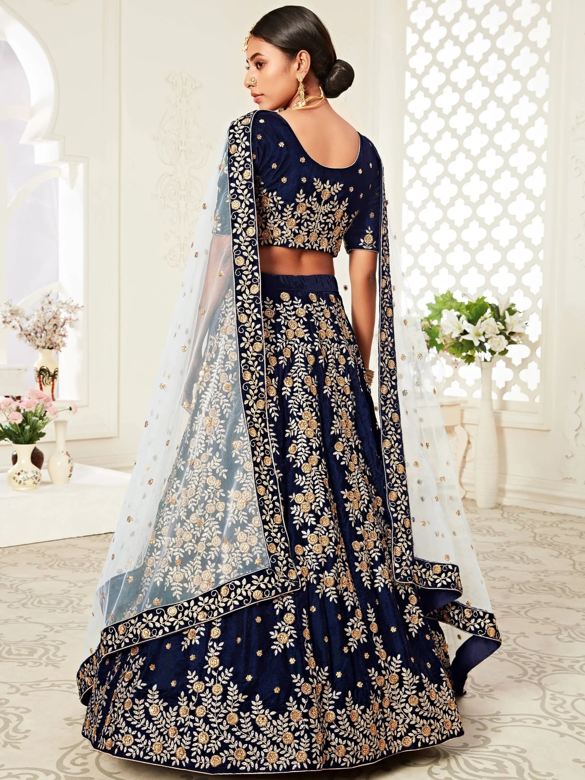Woman in a navy blue designer lehenga choli with gold embroidery and a sheer dupatta.