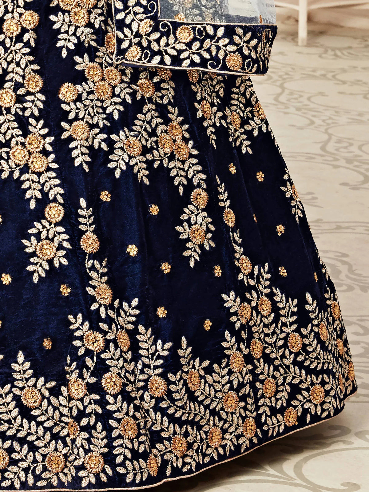 Close-up of a navy blue velvet lehenga with intricate gold floral embroidery.