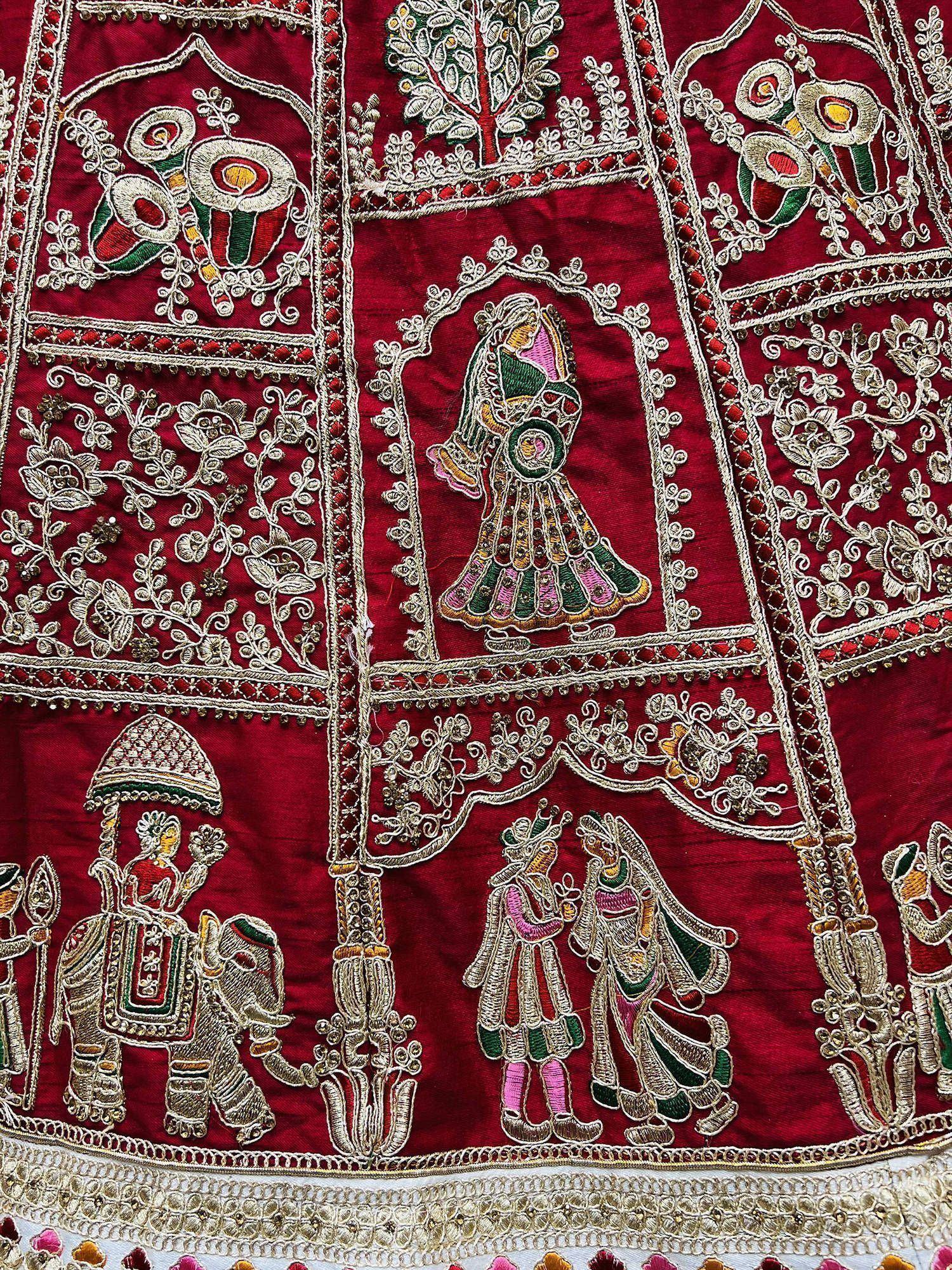 Richly embroidered red Indian ethnic wear with traditional motifs, figures, and floral patterns for festive occasions.