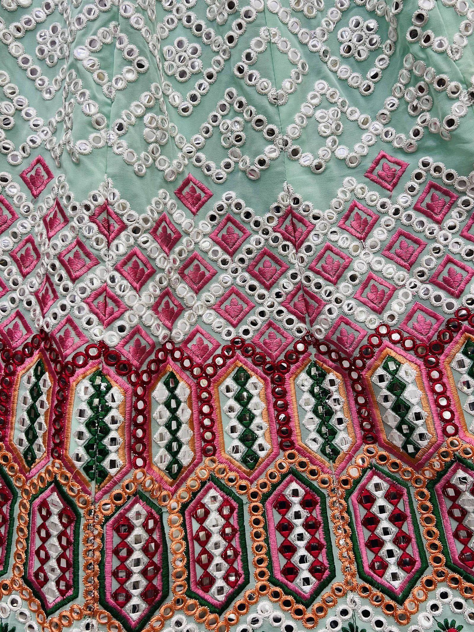 Mint green ethnic wear with intricate mirror work, pink and red embroidery, and geometric patterns.