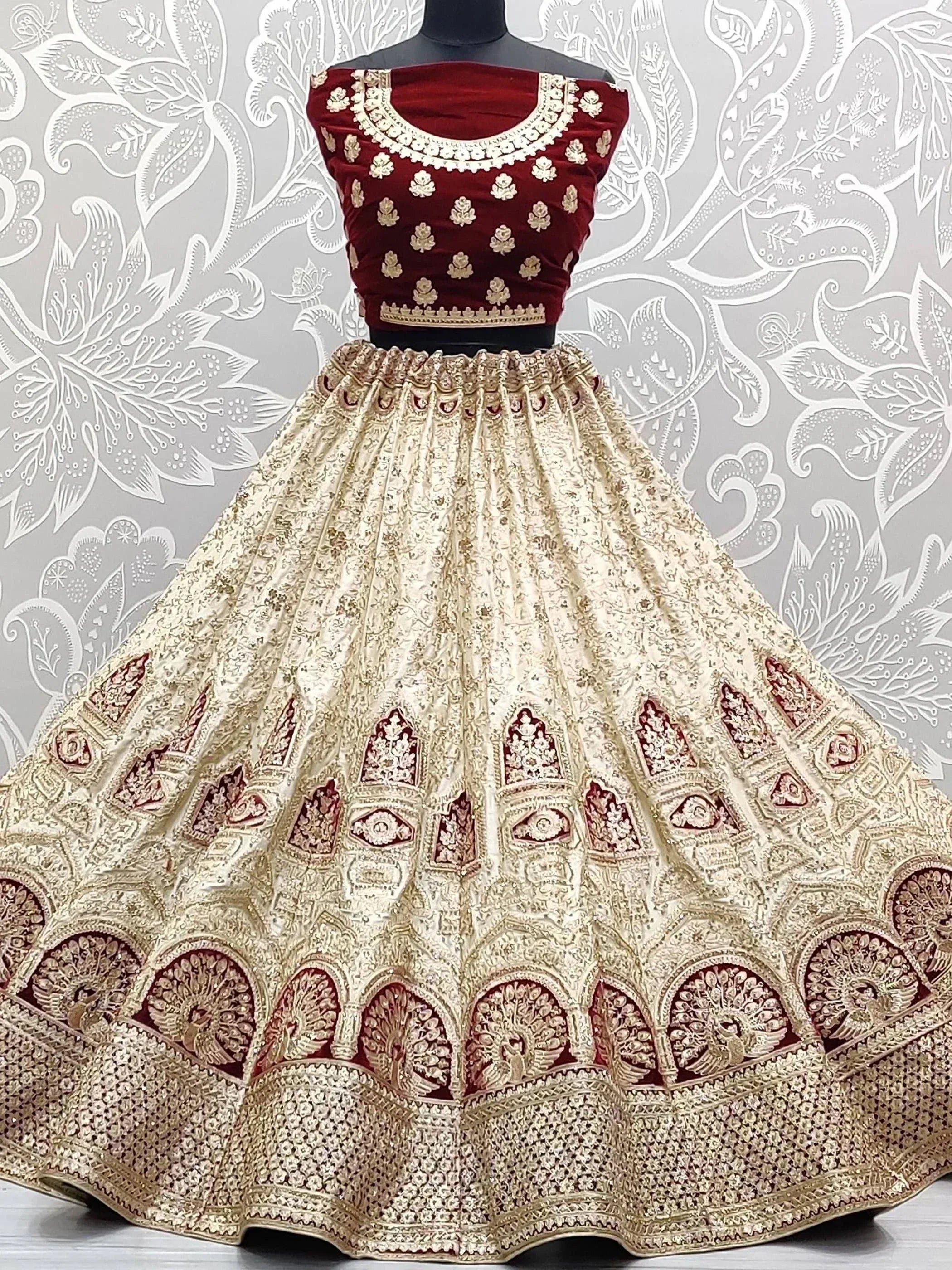 Maroon velvet blouse with gold embroidery paired with cream lehenga featuring peacock motifs, ideal for Indian weddings.