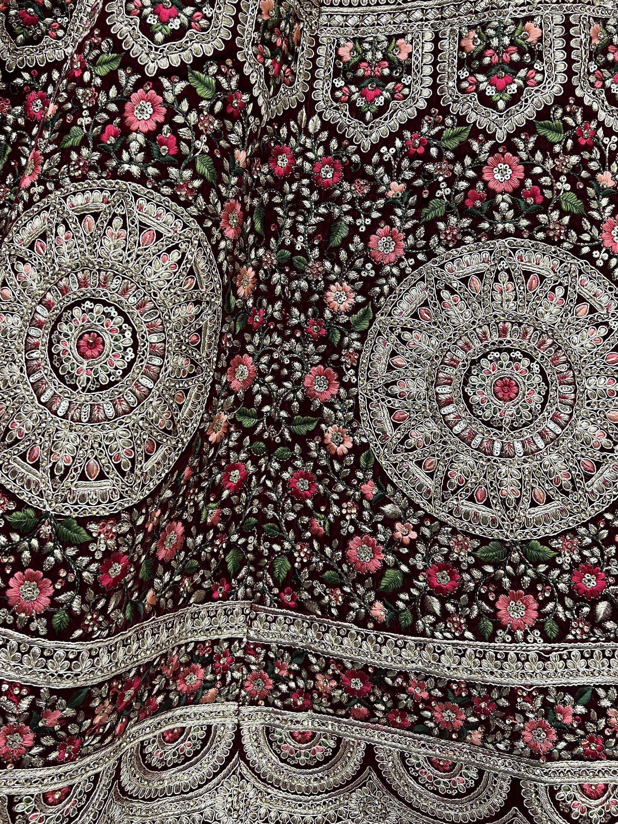 Richly embroidered Indian ethnic wear fabric with floral and paisley motifs in deep red and gold.