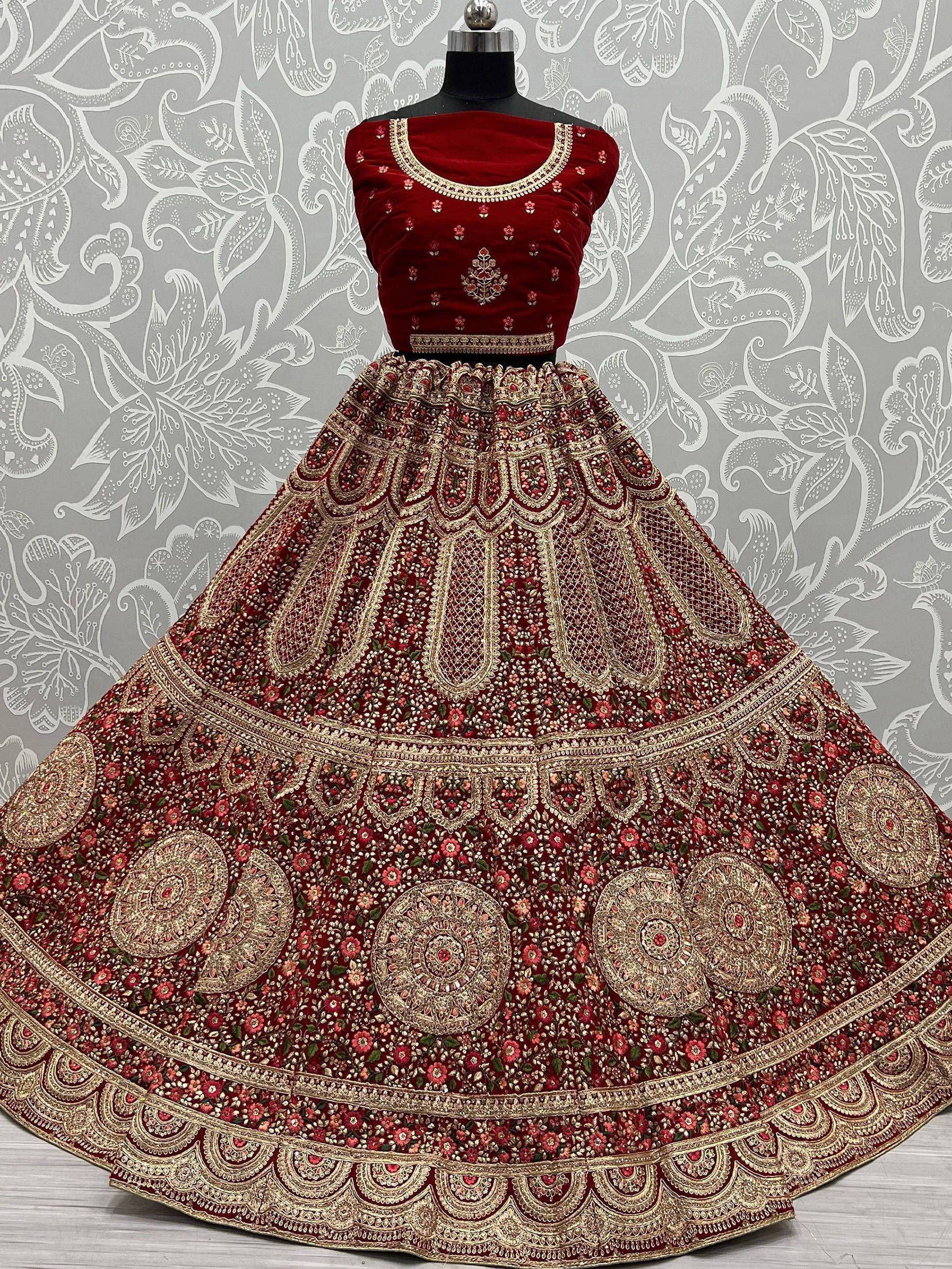 Red velvet designer lehenga choli with heavy gold embroidery and floral motifs, perfect for Indian weddings.