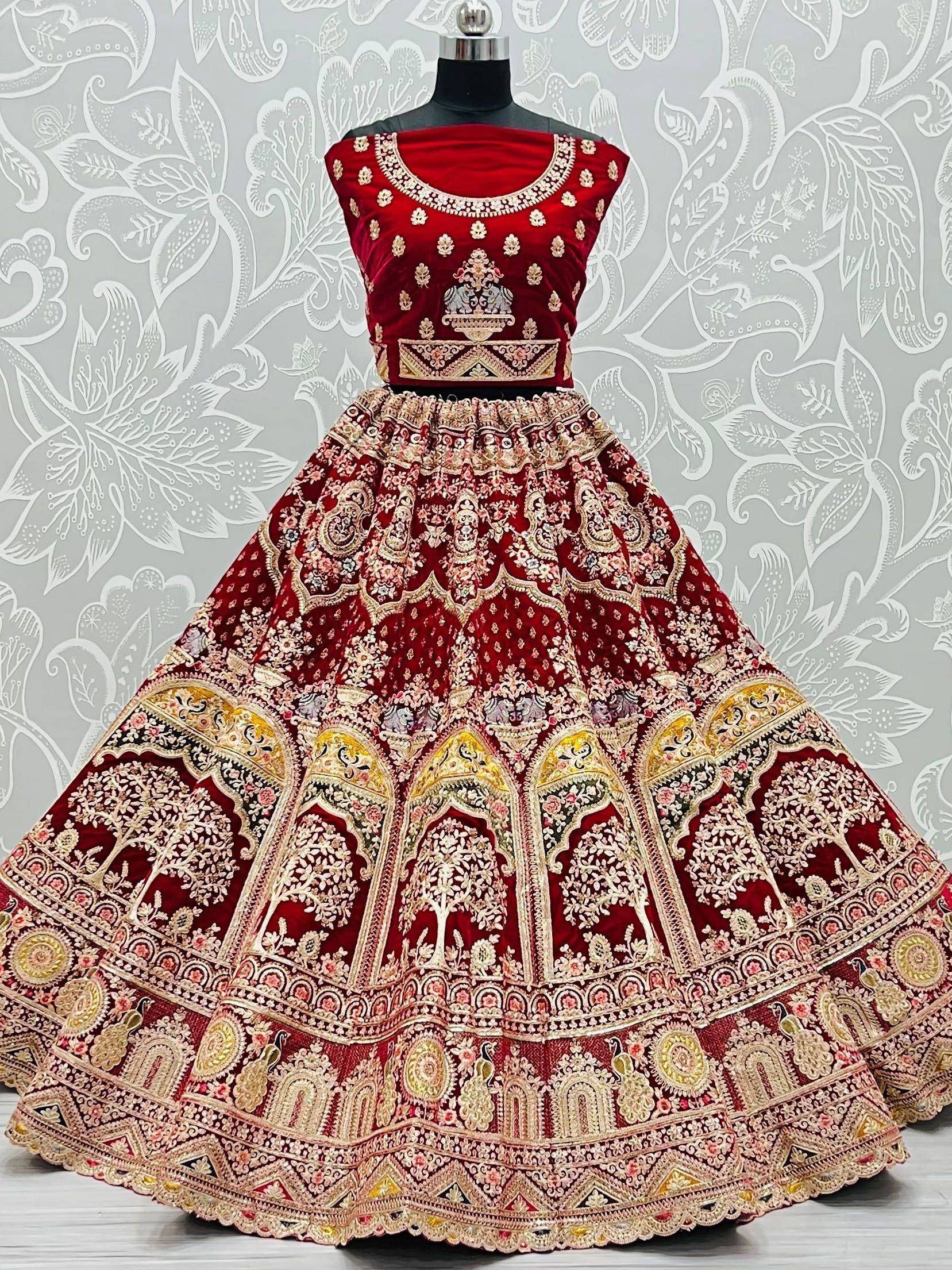 Red velvet designer lehenga choli with heavy gold embroidery and floral motifs, perfect for Indian weddings.