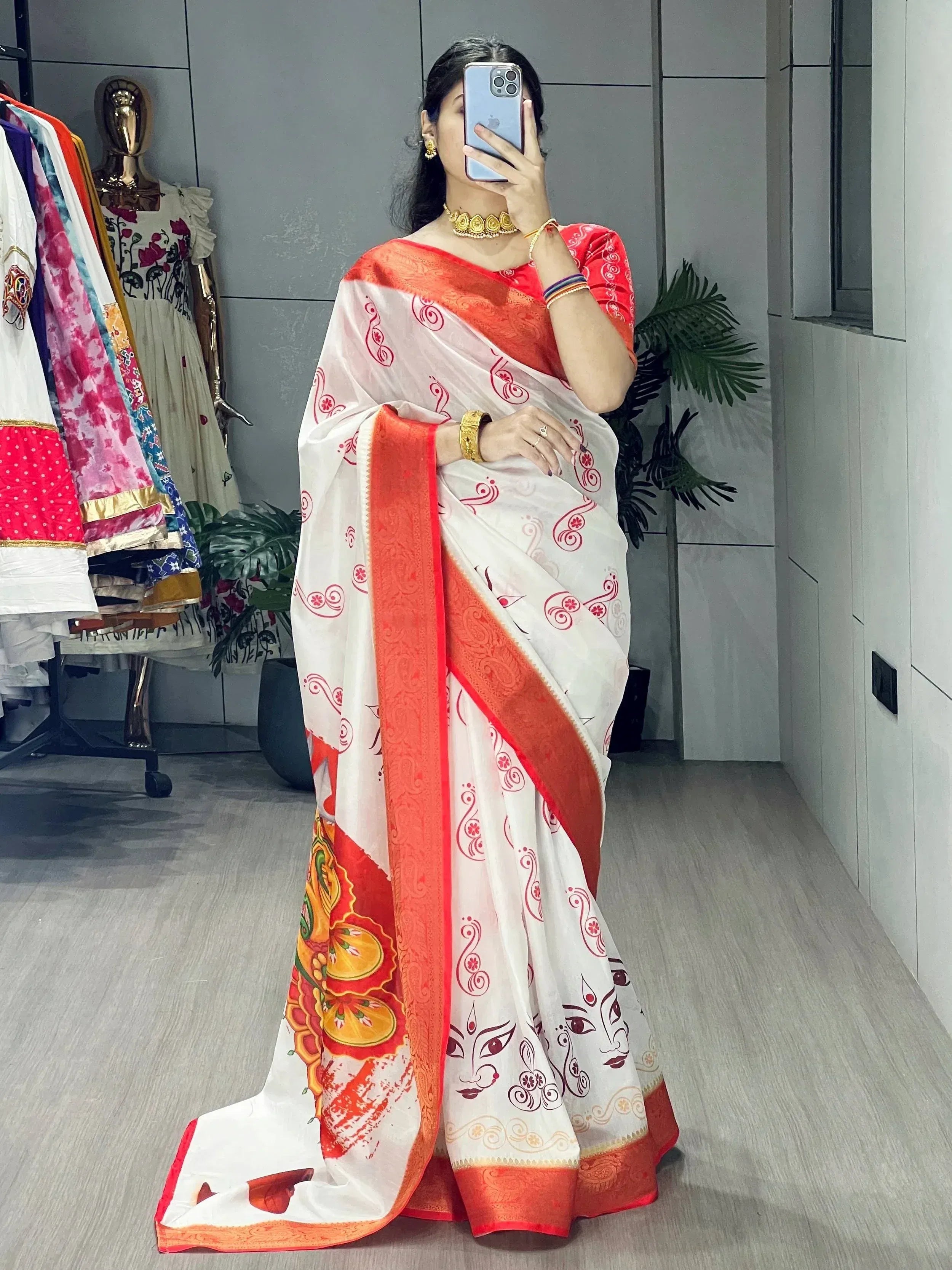 White saree with red border and printed motifs, paired with gold jewelry, perfect for ethnic occasions.