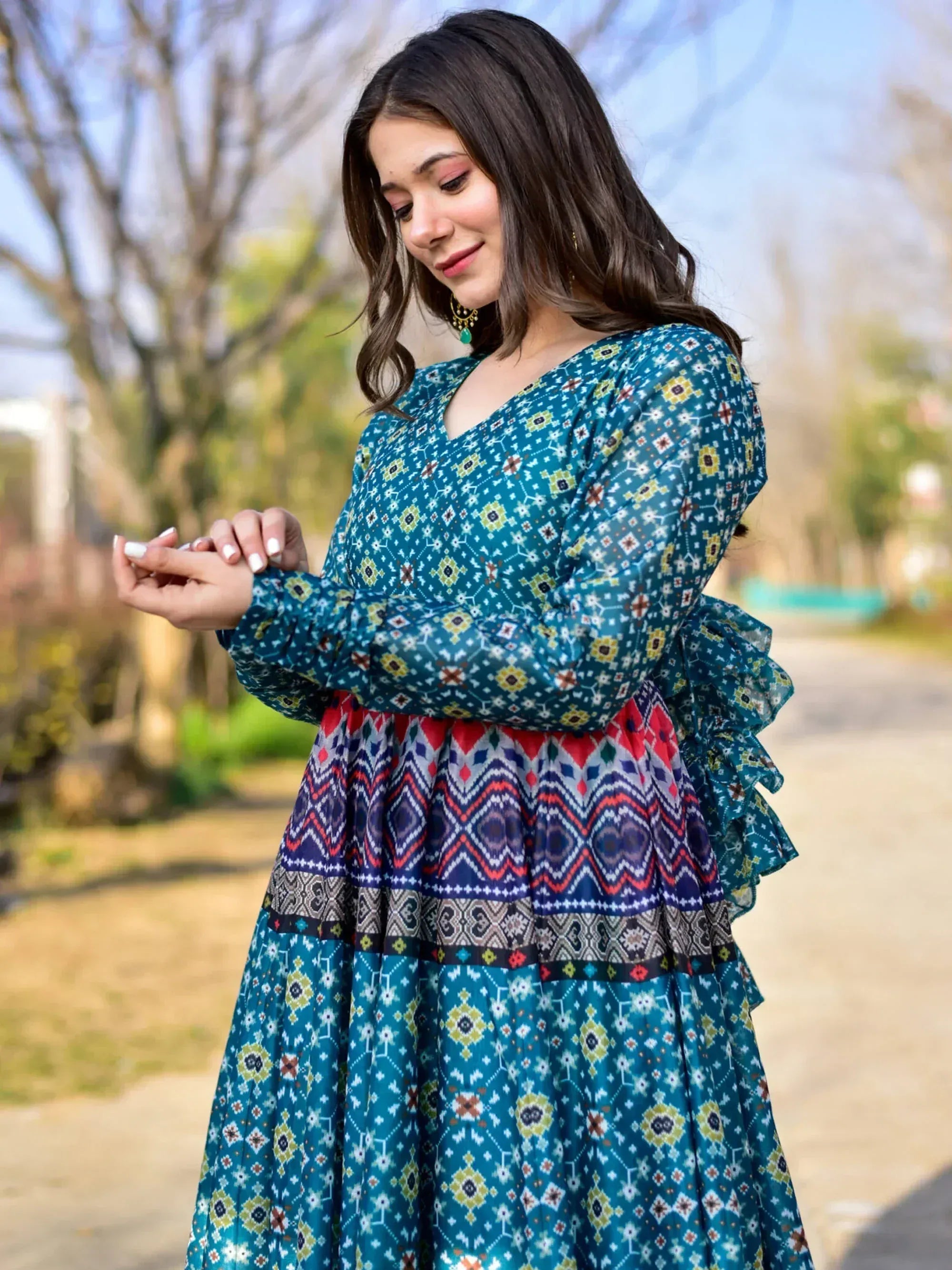 Woman in teal printed ethnic gown with ruffled sleeves and geometric patterns, perfect for festive occasions.