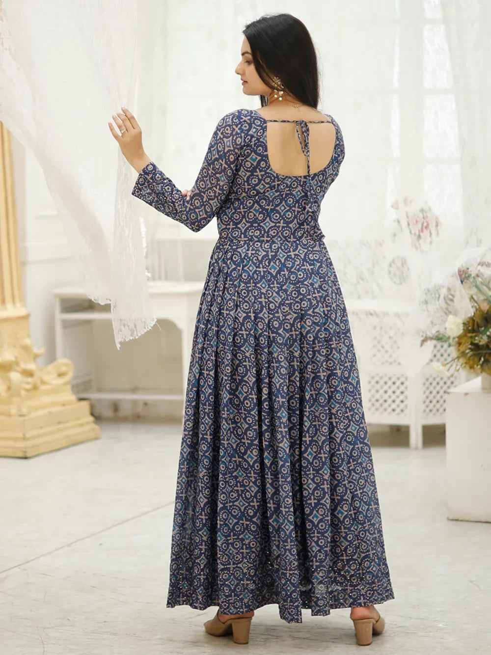 Woman in navy blue printed ethnic gown with open back and long sleeves, standing indoors