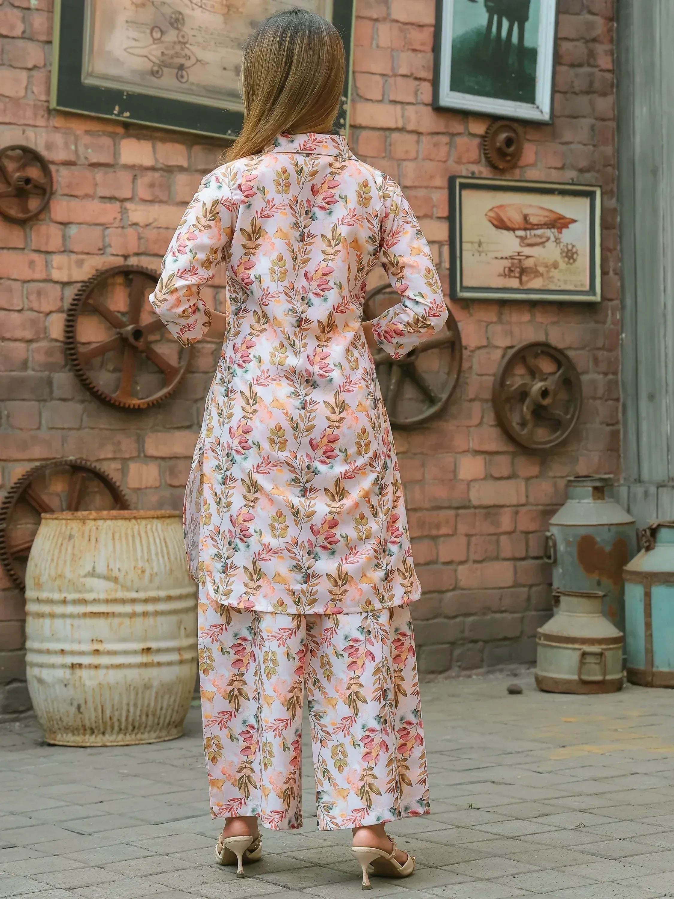 Woman wearing floral printed kurta and palazzo set, standing outdoors against a brick wall