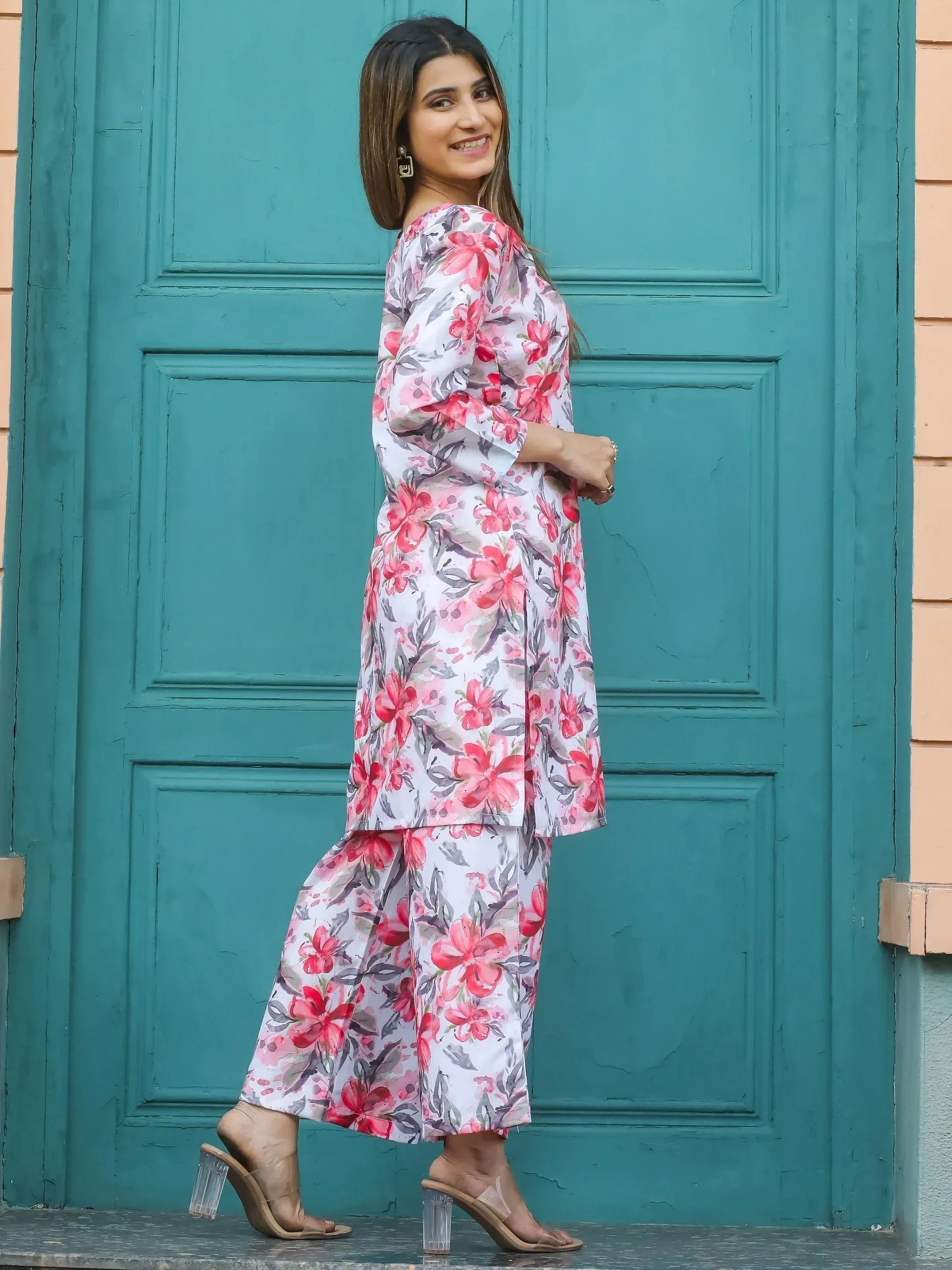 Floral print salwar kameez with pink and red blooms, styled with clear heels against teal door