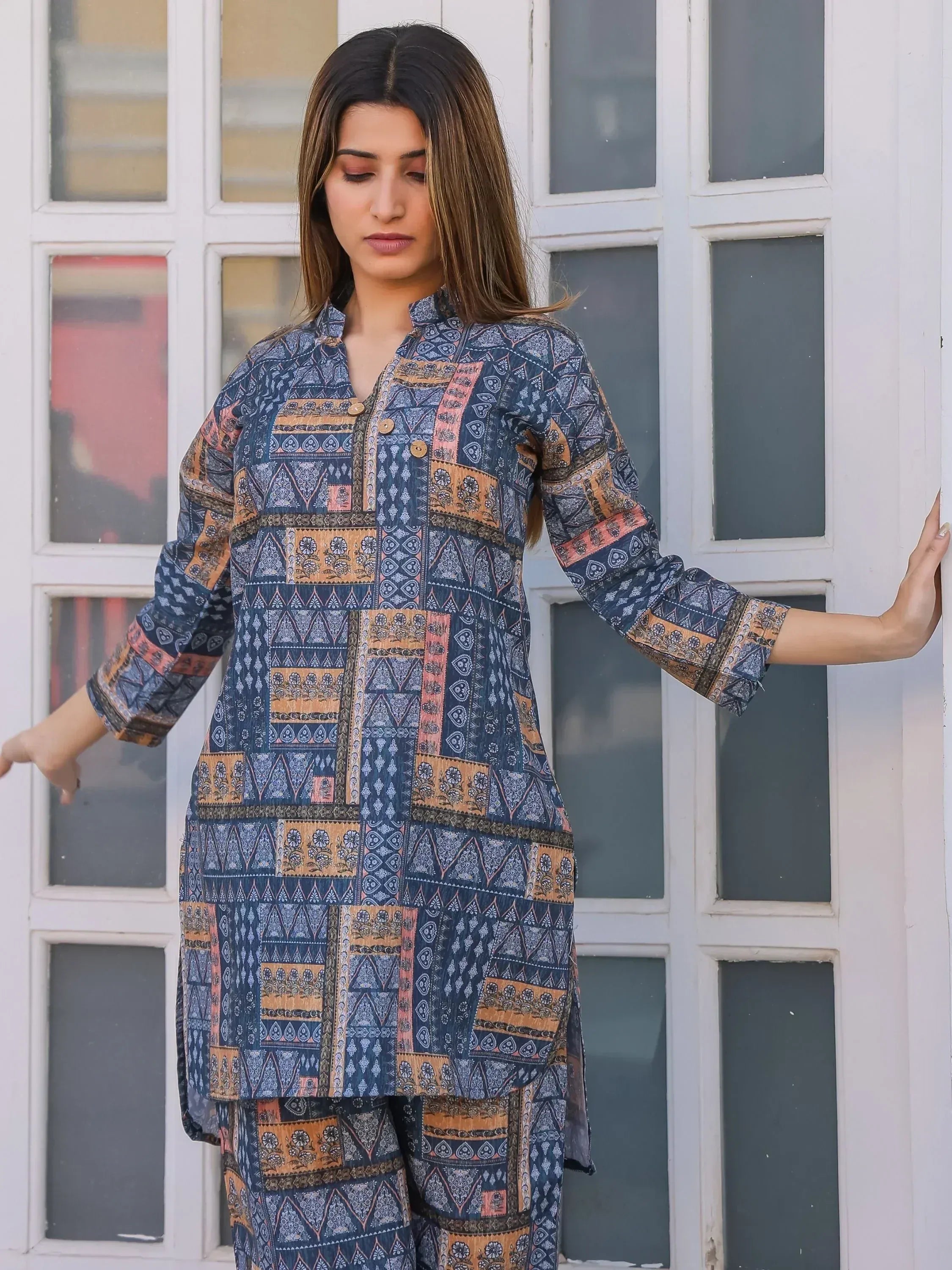 Woman in blue and orange printed ethnic kurti with matching pants, standing by white paneled door