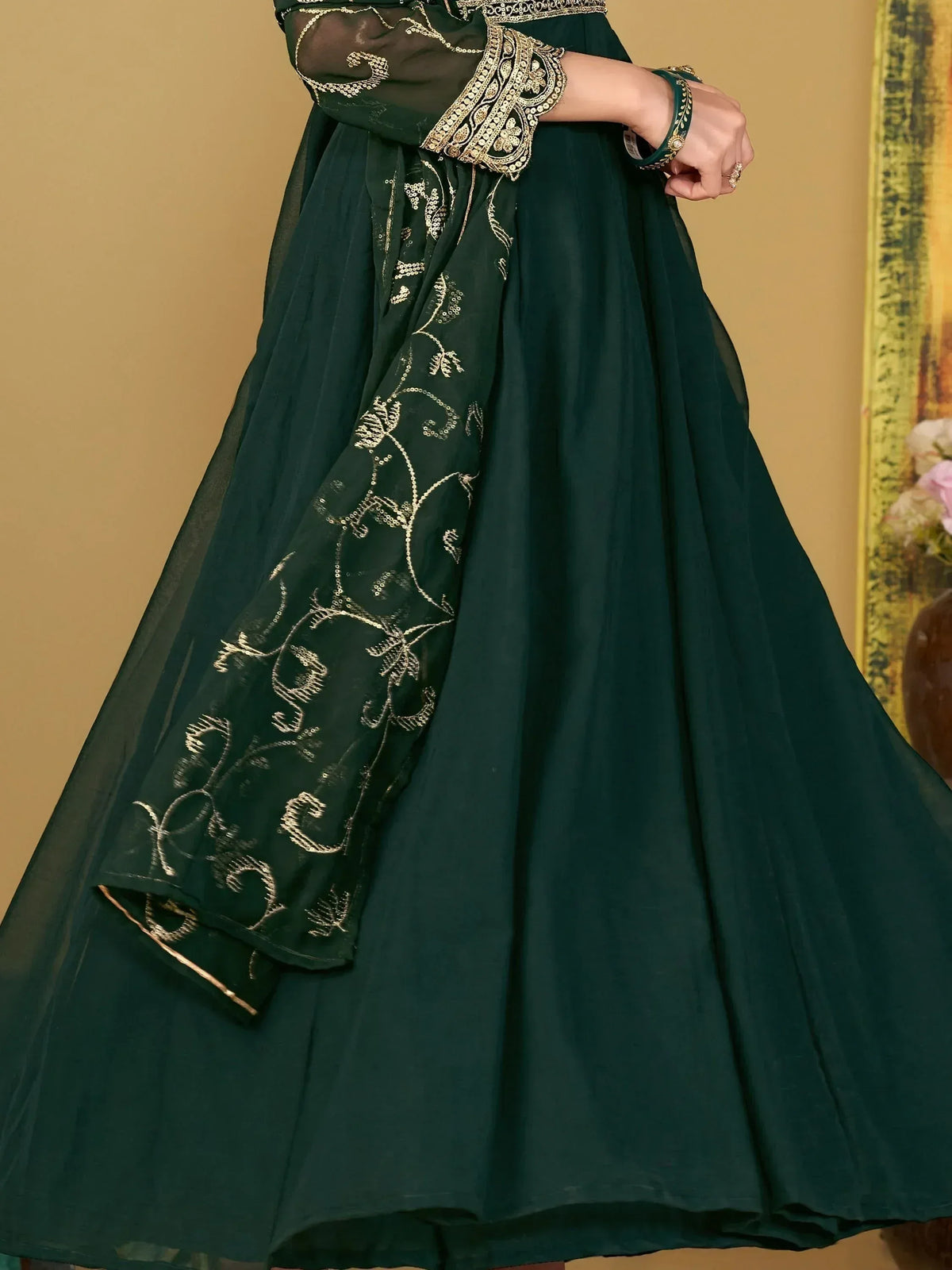 Emerald green ethnic gown with gold embroidery and sheer dupatta, perfect for Indian festive occasions.