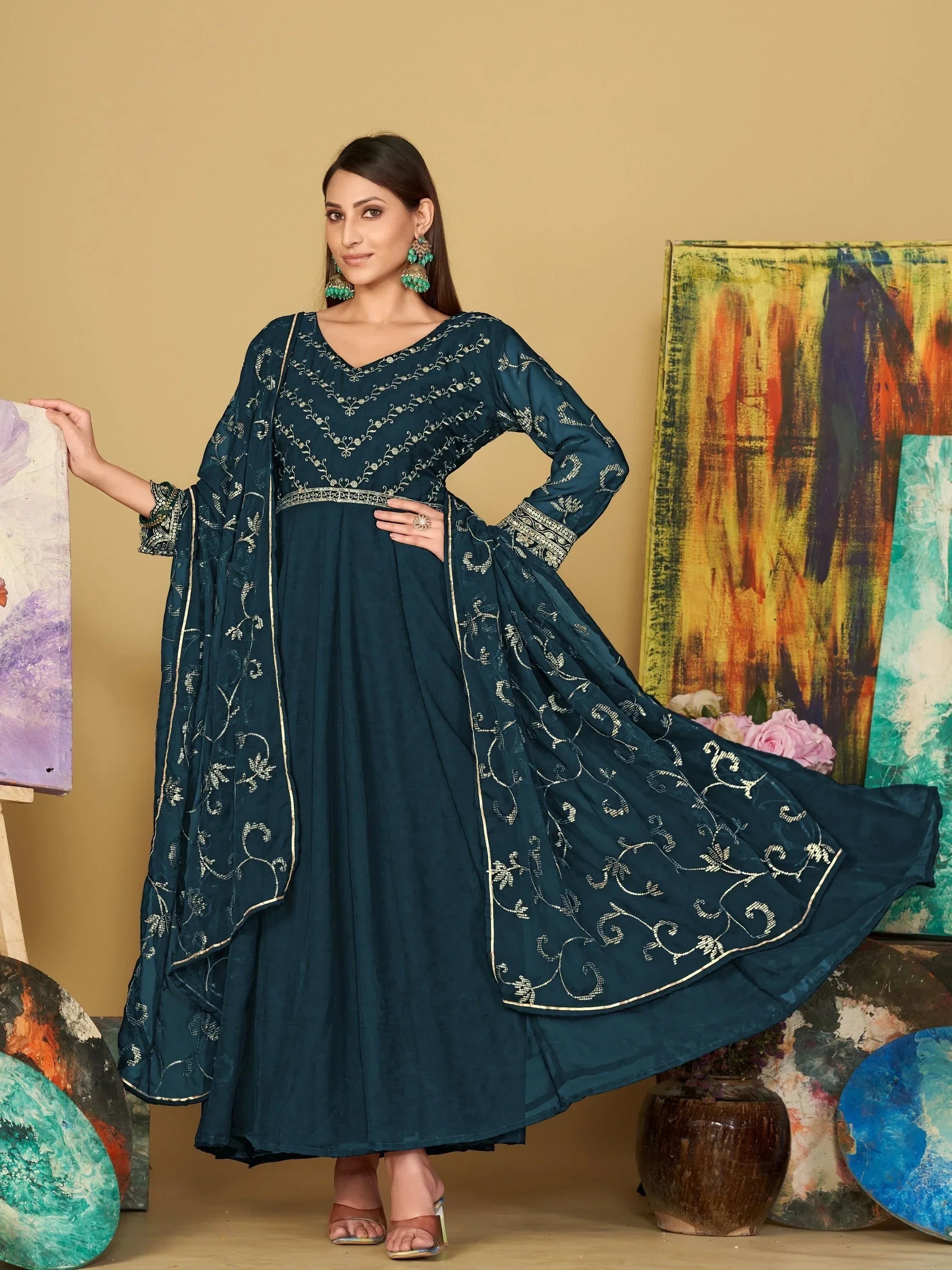 Woman in navy blue embroidered ethnic gown with dupatta, standing by colorful paintings