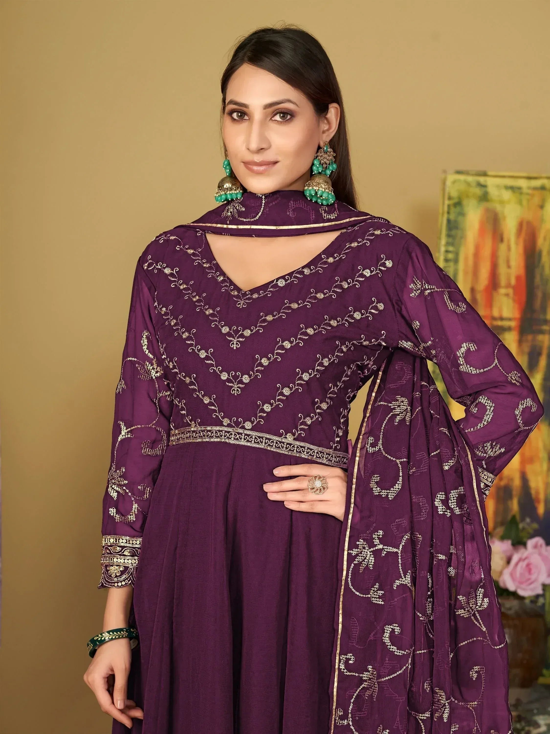 Purple embroidered ethnic gown with gold detailing, paired with matching dupatta and green jewelry