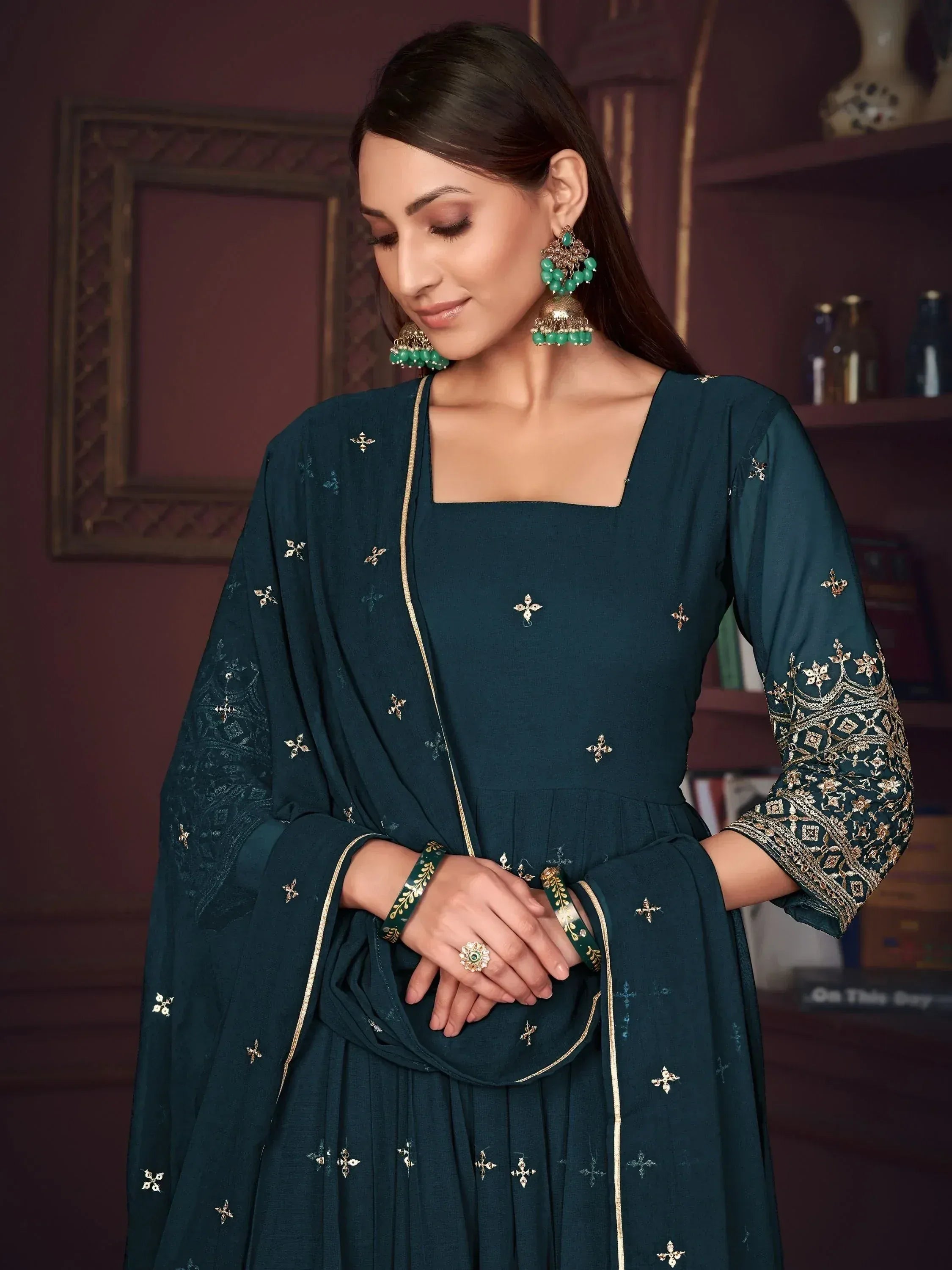 Teal embroidered salwar kameez with gold detailing, paired with matching green jewelry for ethnic wear.