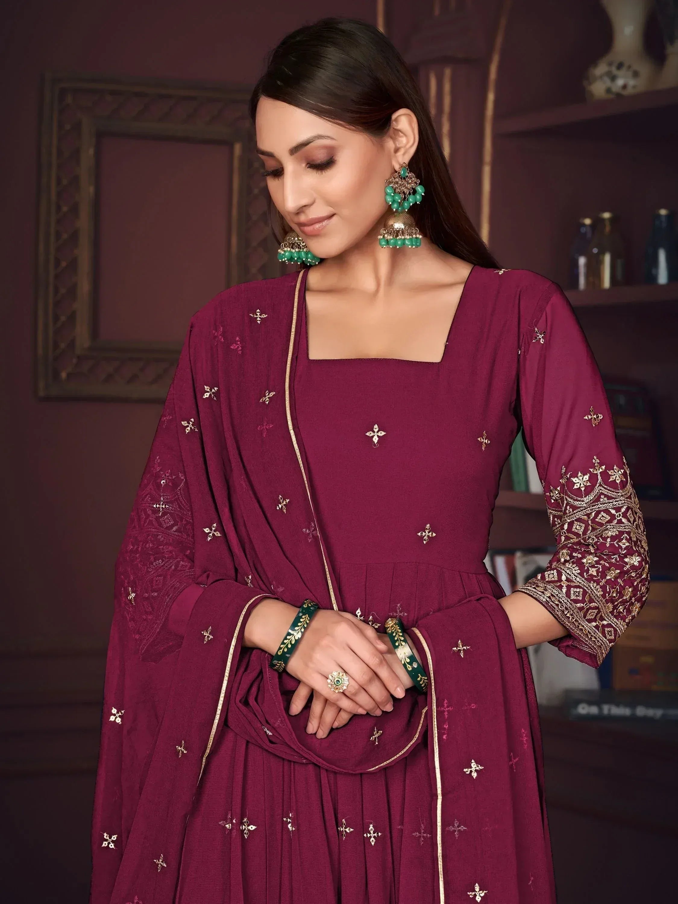 Elegant maroon salwar kameez with gold embroidery and matching dupatta, styled with green jewelry for festive occasions