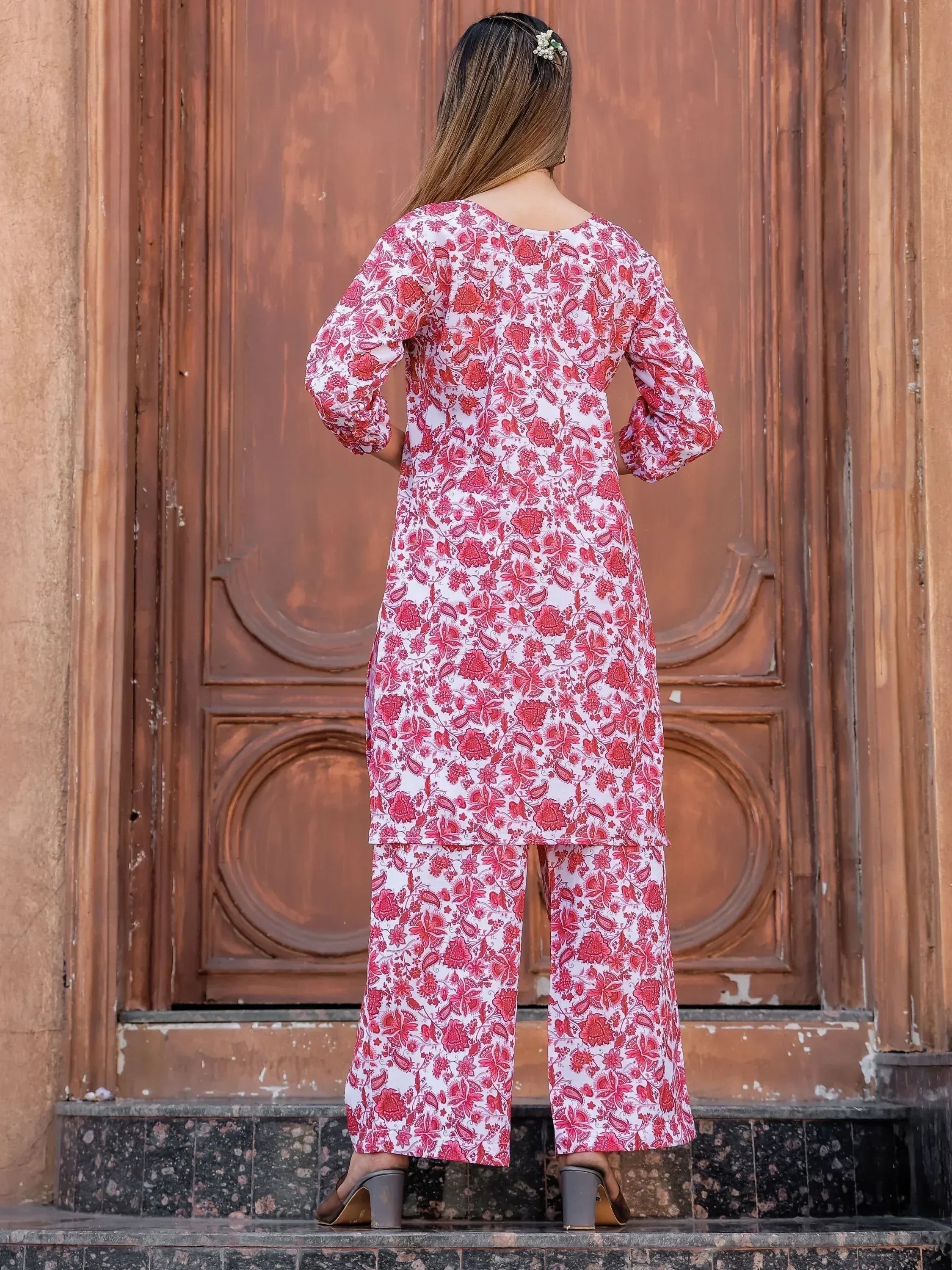 Woman in red floral print salwar kameez standing before wooden door, ethnic wear outfit