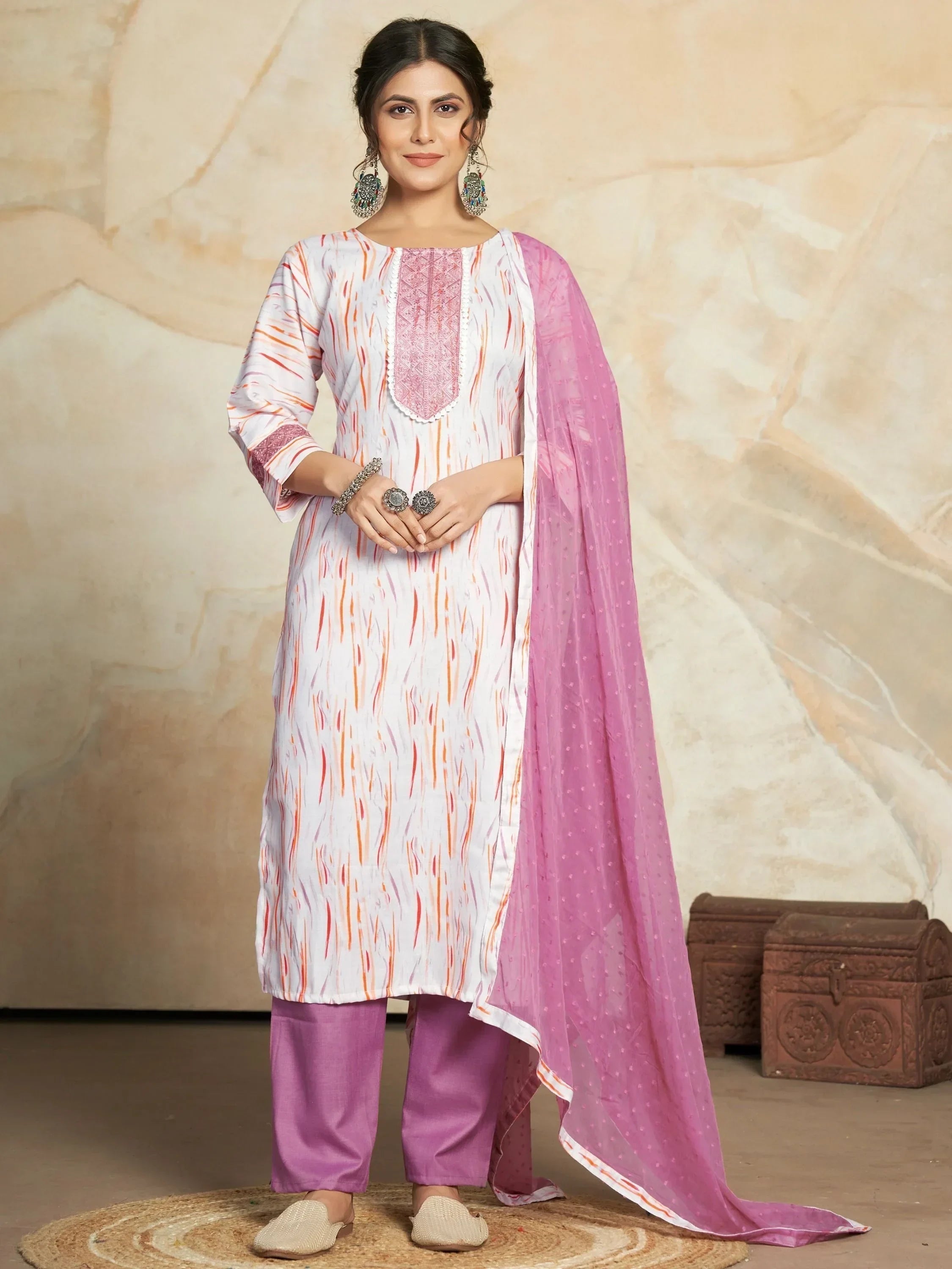 Woman wearing a printed salwar kameez with pink dupatta, ethnic jewelry, and flat shoes