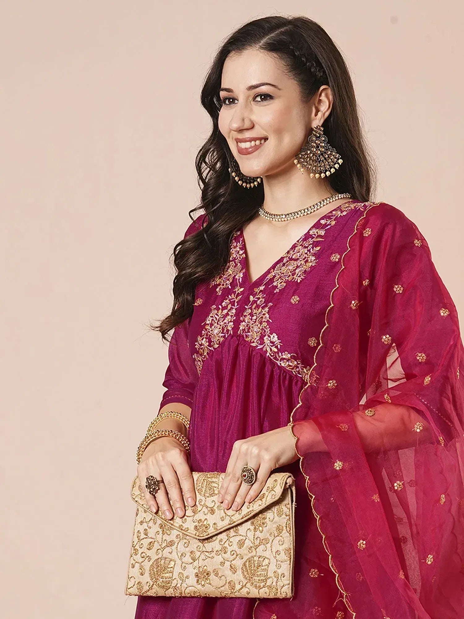 Woman in maroon embroidered ethnic gown with gold detailing, matching dupatta, and traditional jewelry