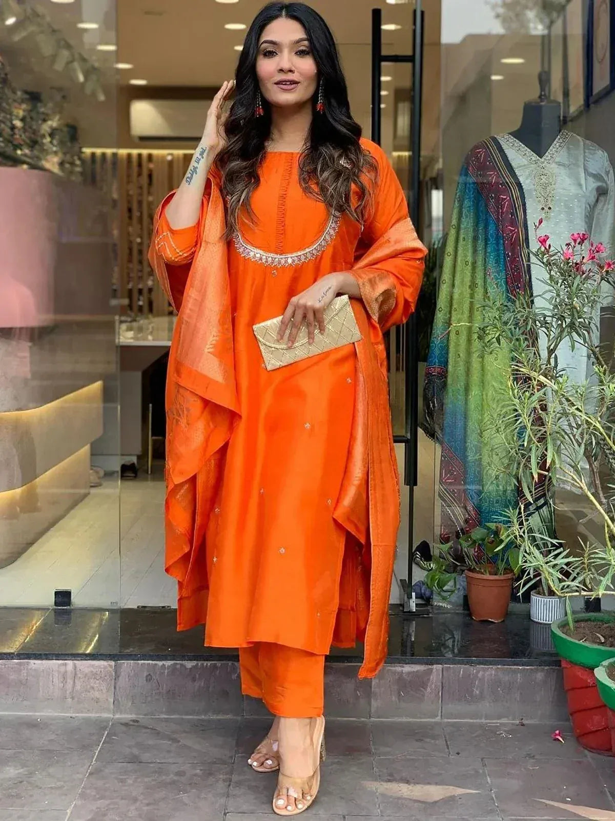 Vibrant orange ethnic salwar kameez with embellished neckline, paired with matching dupatta and clutch, perfect for festive occasions.