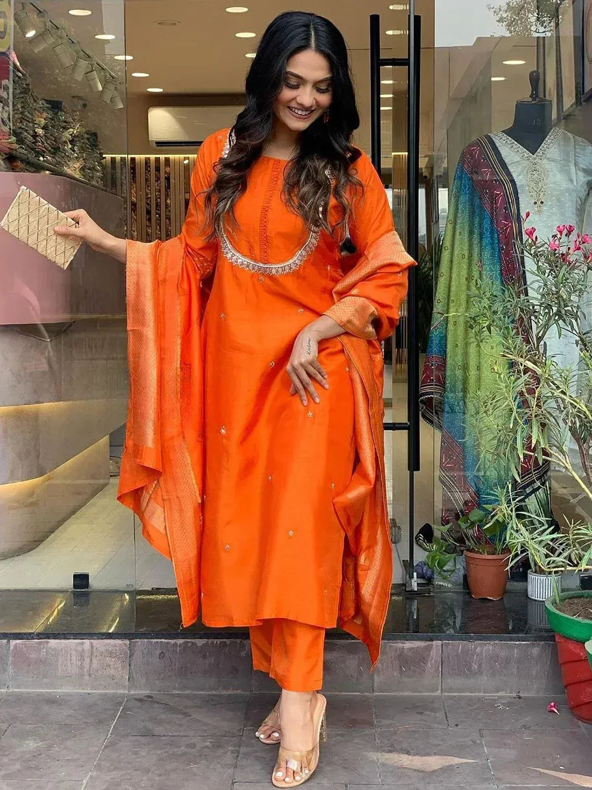 Vibrant orange salwar kameez with embroidered neckline, paired with matching dupatta and heels, perfect for festive occasions.