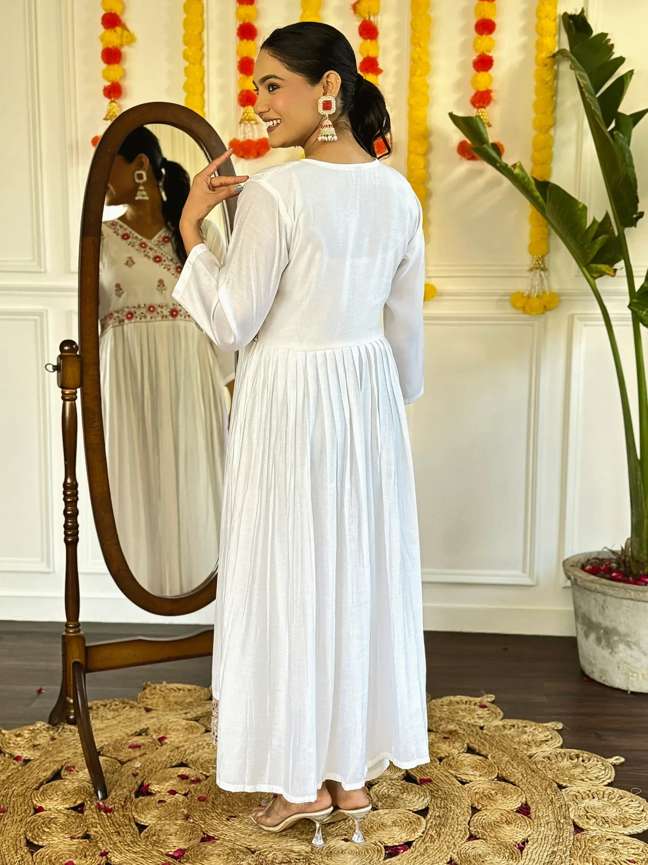 White ethnic gown with pleated skirt, mirror reflection, festive decor, traditional Indian wear