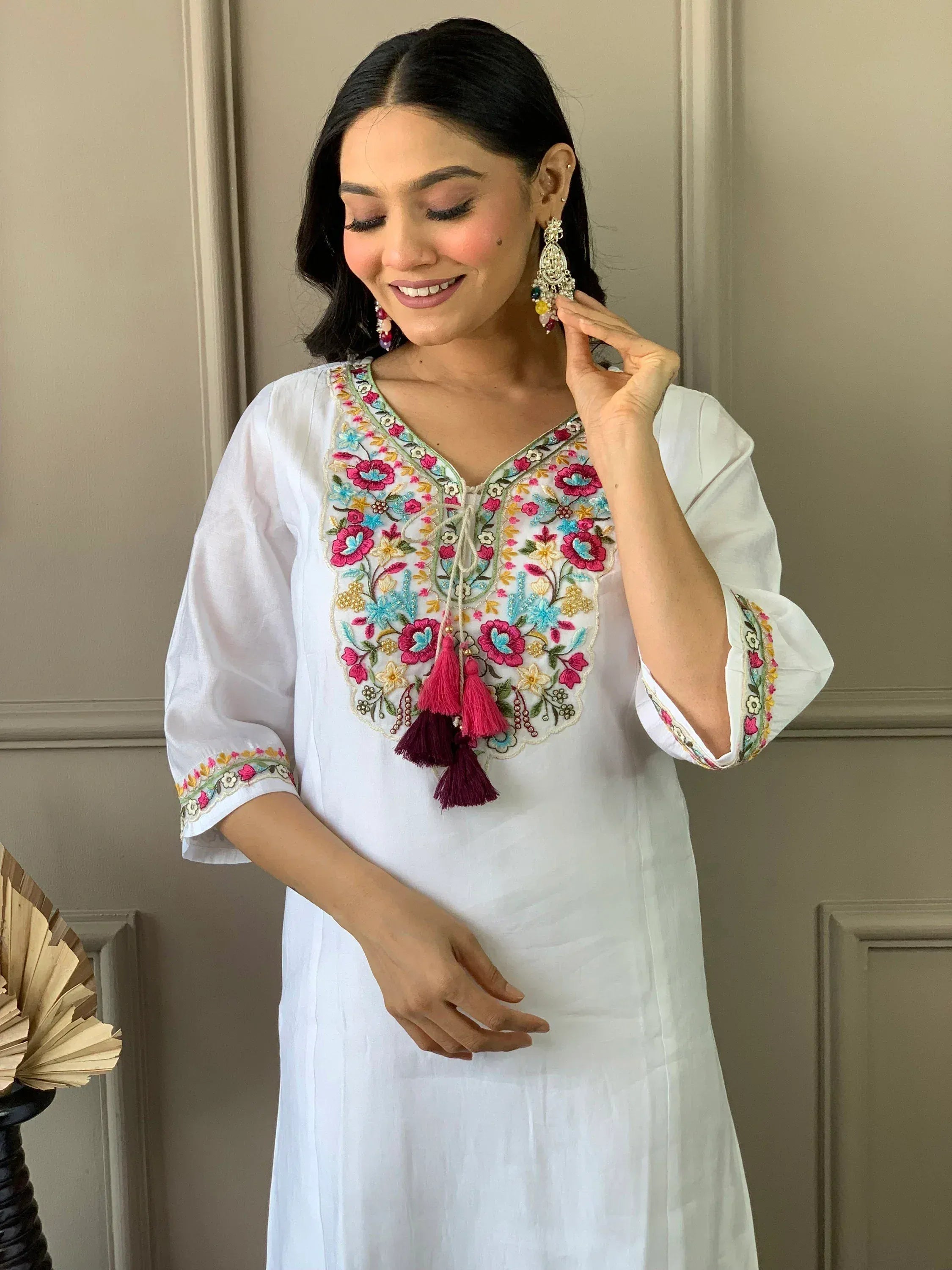 White ethnic kurti with colorful floral embroidery and tassels, paired with statement earrings