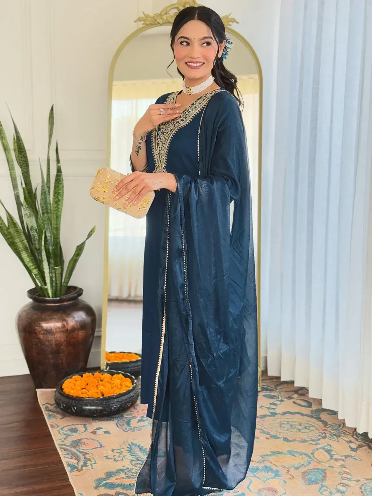 Woman in navy blue embroidered ethnic gown with gold detailing, holding clutch, ideal for Indian occasions