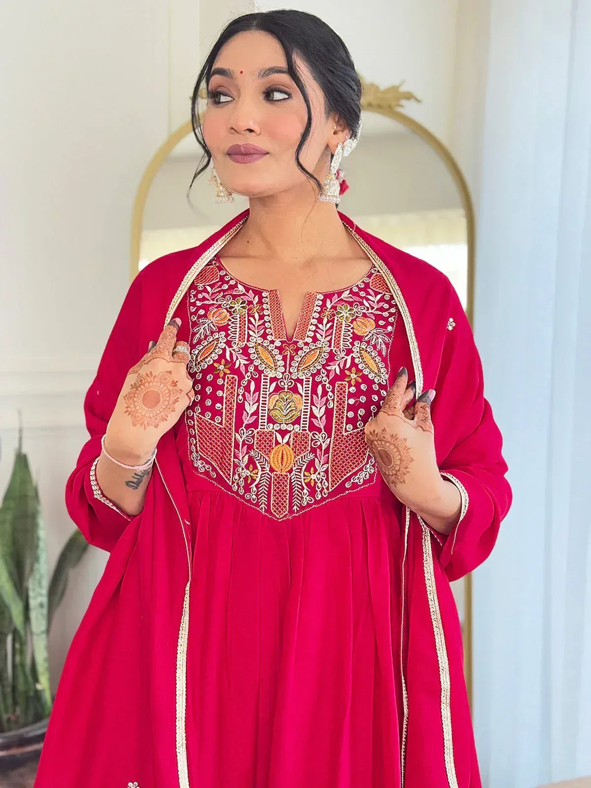 Woman in vibrant red ethnic gown with intricate embroidery and henna hands, perfect for festive occasions.