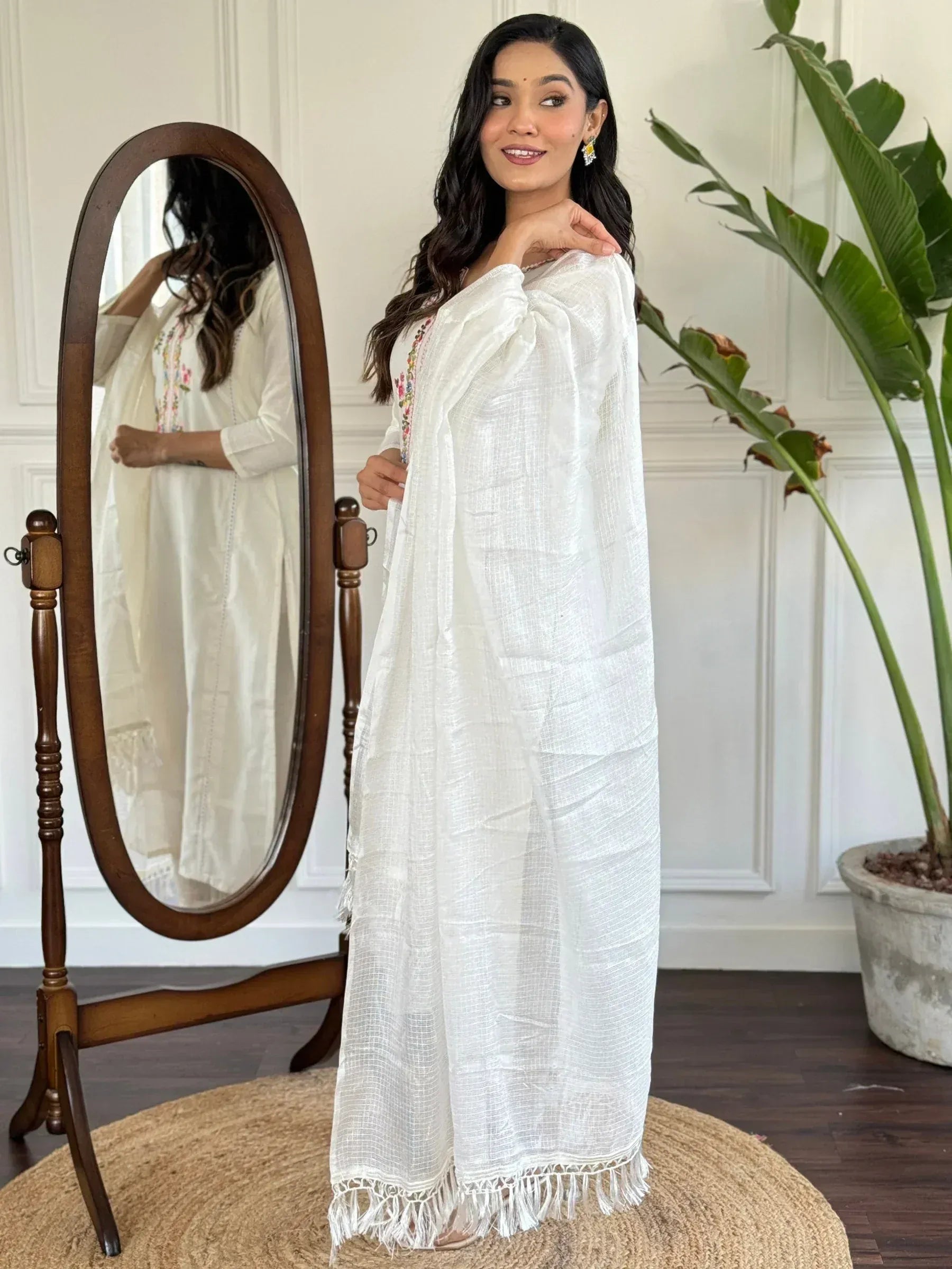White embroidered ethnic gown with fringe hem, styled with mirror and indoor plant