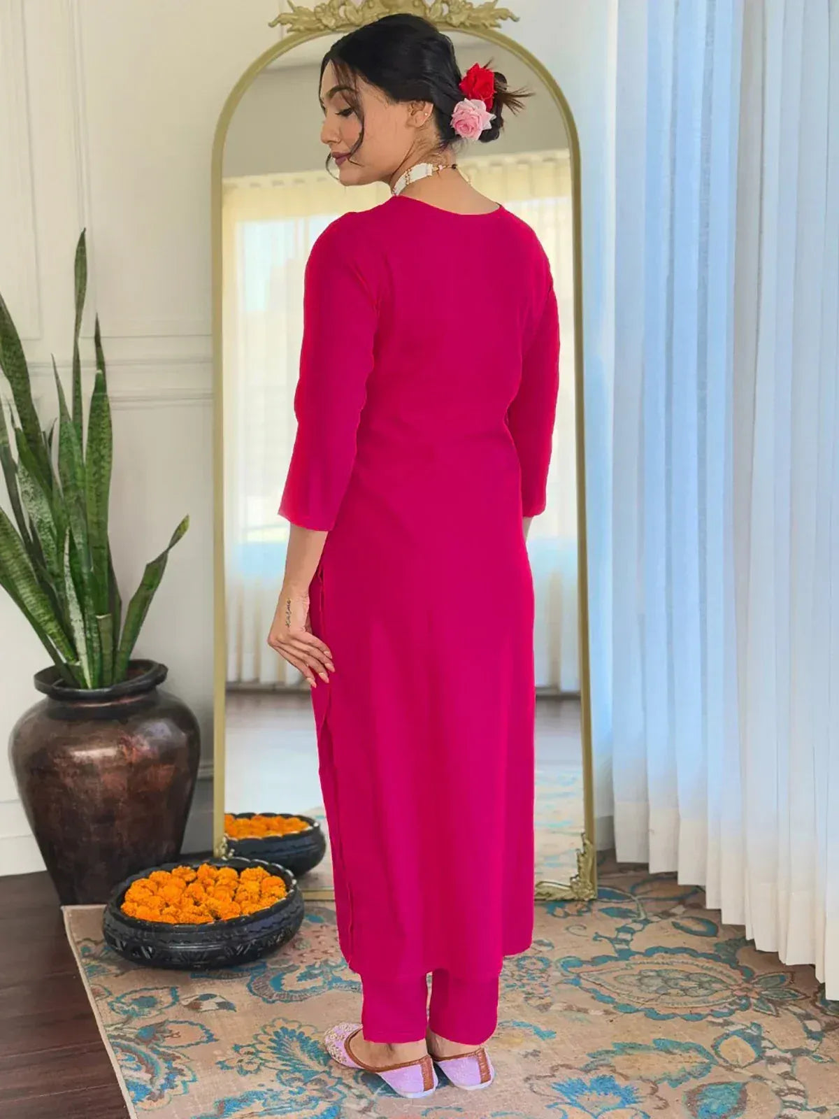Woman in vibrant pink ethnic kurta with matching pants, floral hair accessories, and traditional footwear.