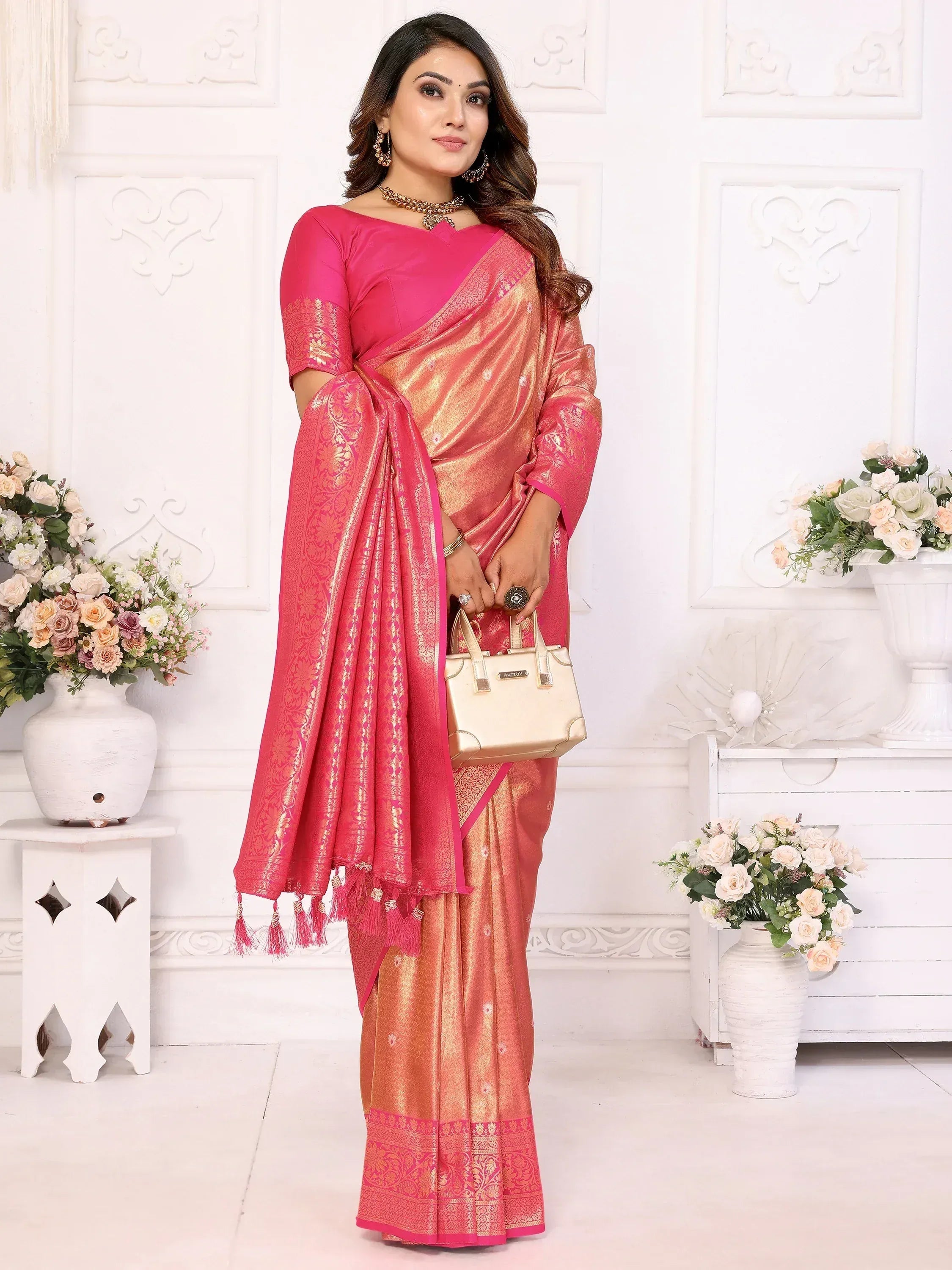 Pink and gold designer saree with intricate embroidery and tassels, paired with a matching blouse and handbag