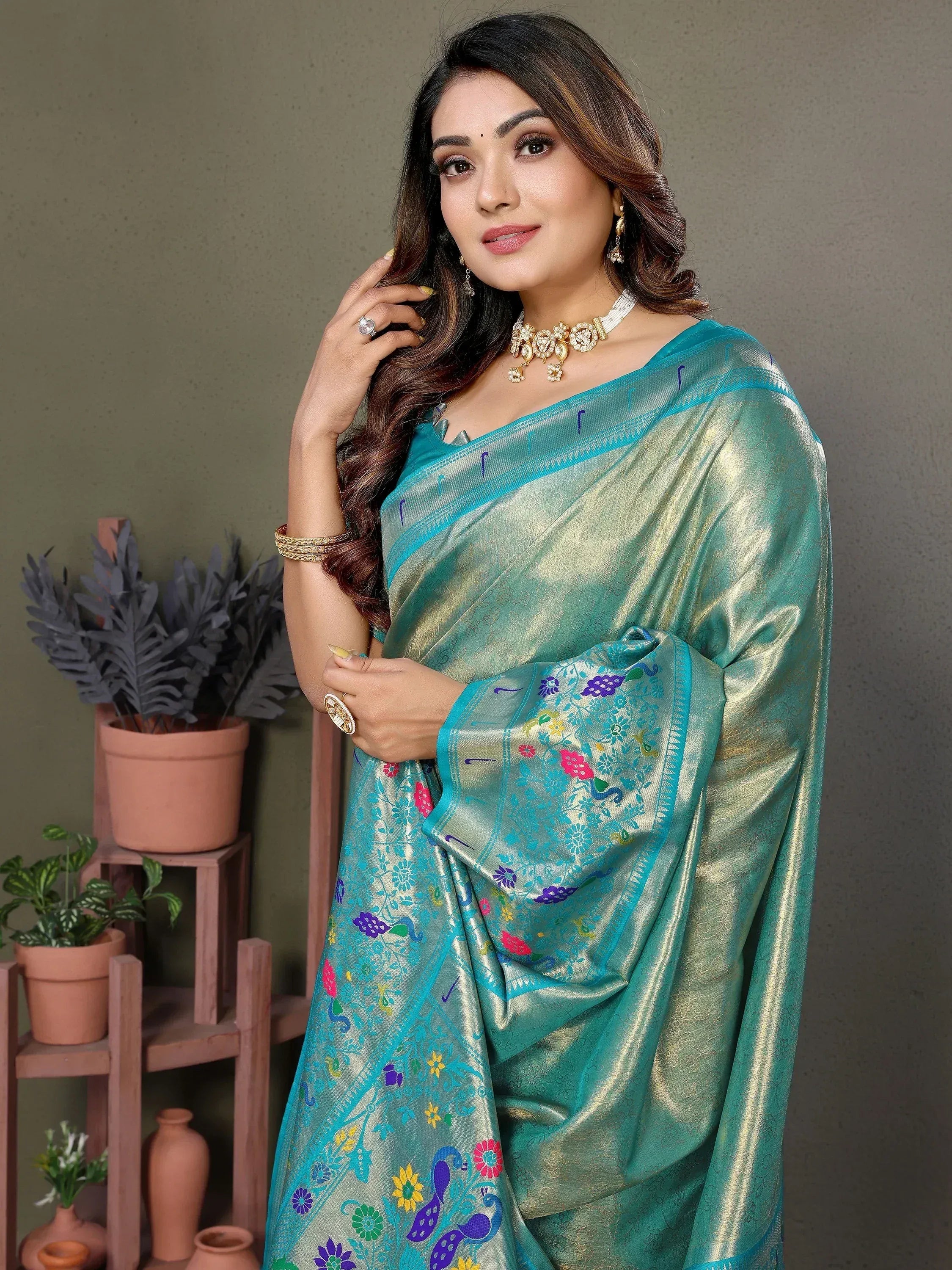 Teal saree with floral and peacock embroidery, paired with gold jewelry for festive occasions