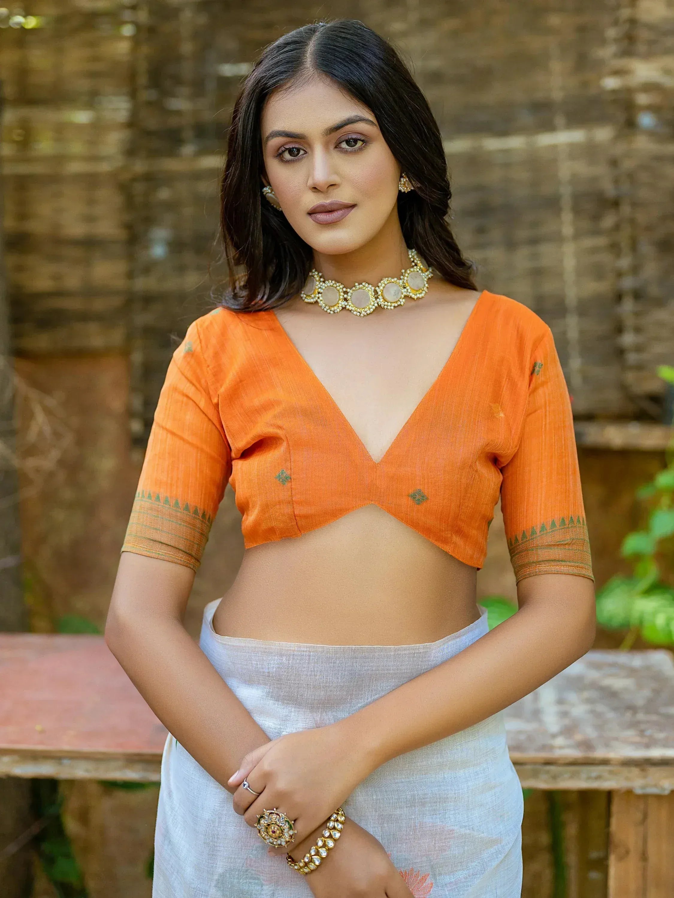 Woman in orange designer blouse and white saree with gold jewelry, ethnic wear