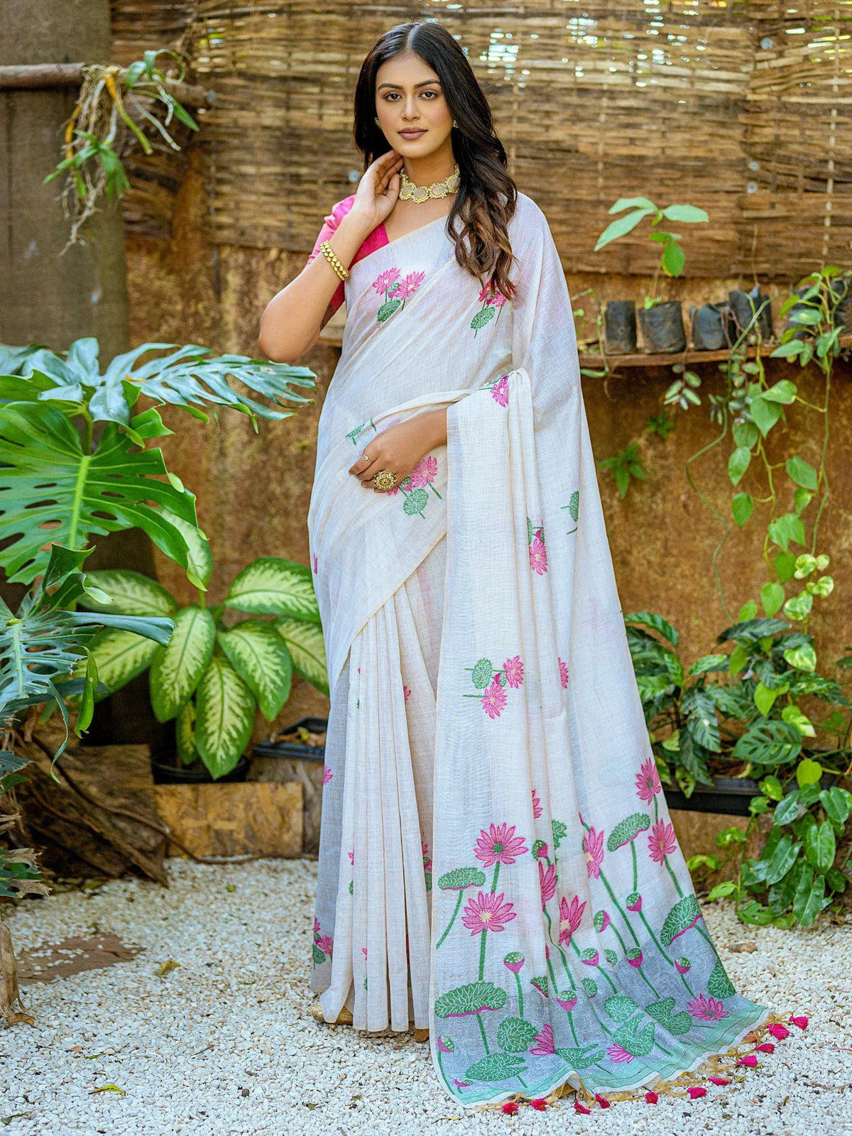 White saree with pink floral print, styled with gold jewelry in a garden setting