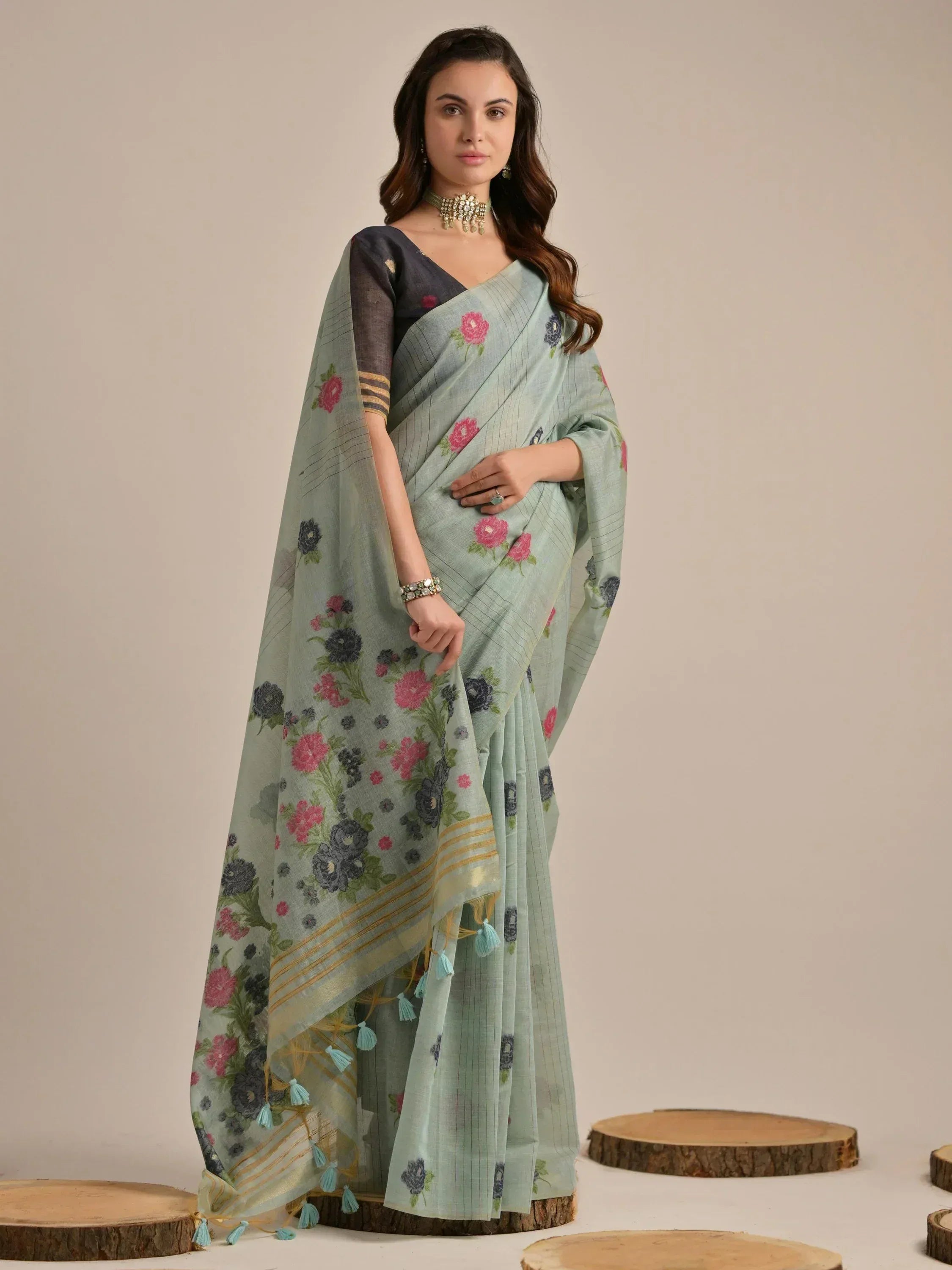 Light green floral saree with pink and blue blooms, gold stripes, and tassels, paired with a black blouse.