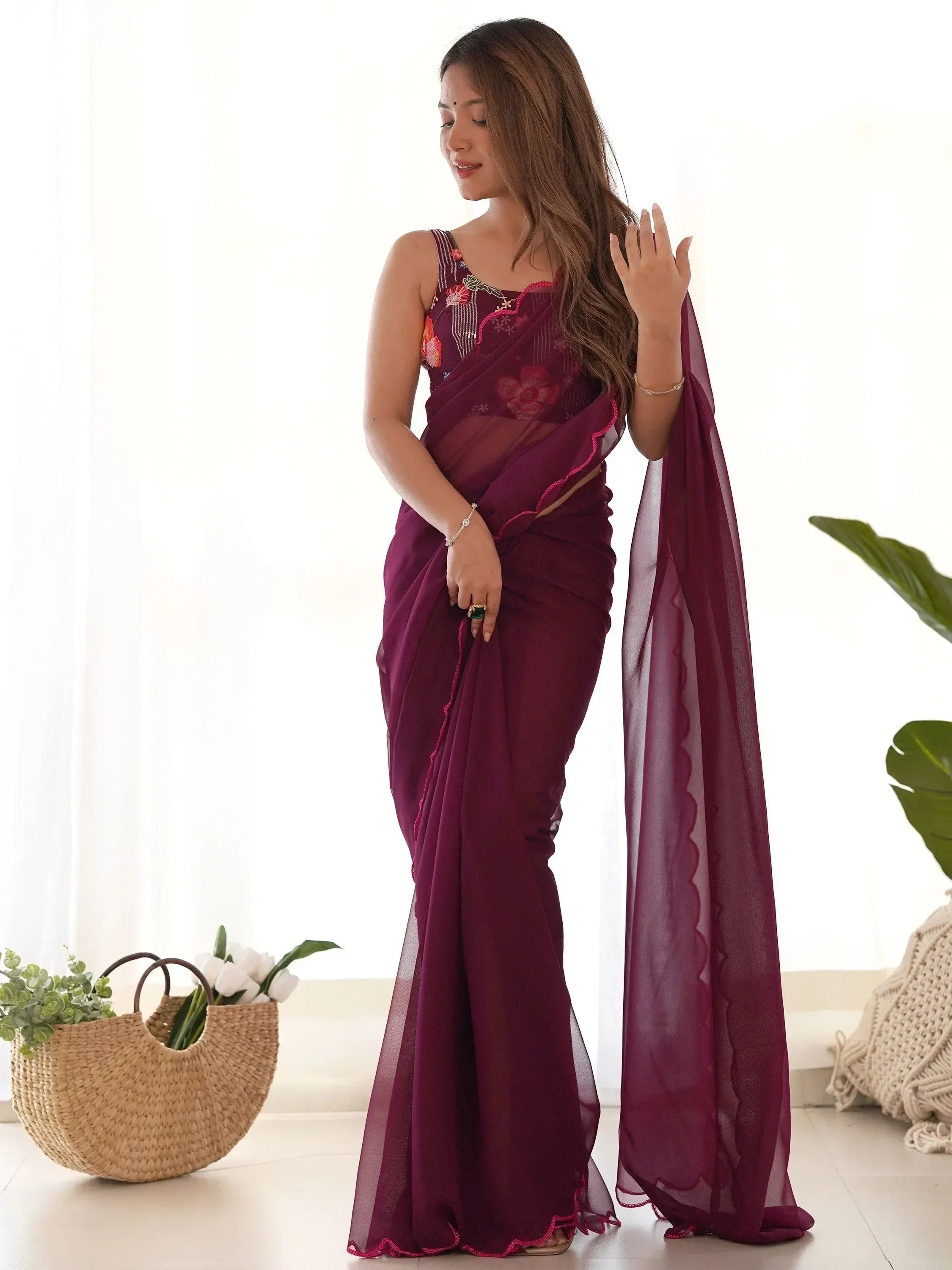 Woman in maroon embroidered saree with floral blouse, sheer dupatta, and scalloped edges, styled for ethnic occasions.
