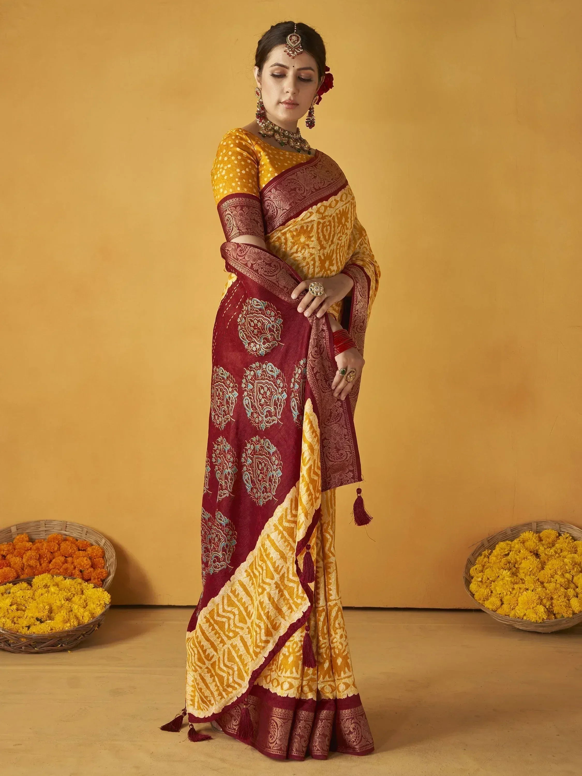 Woman in maroon and yellow designer saree with intricate embroidery, traditional jewelry, and floral baskets