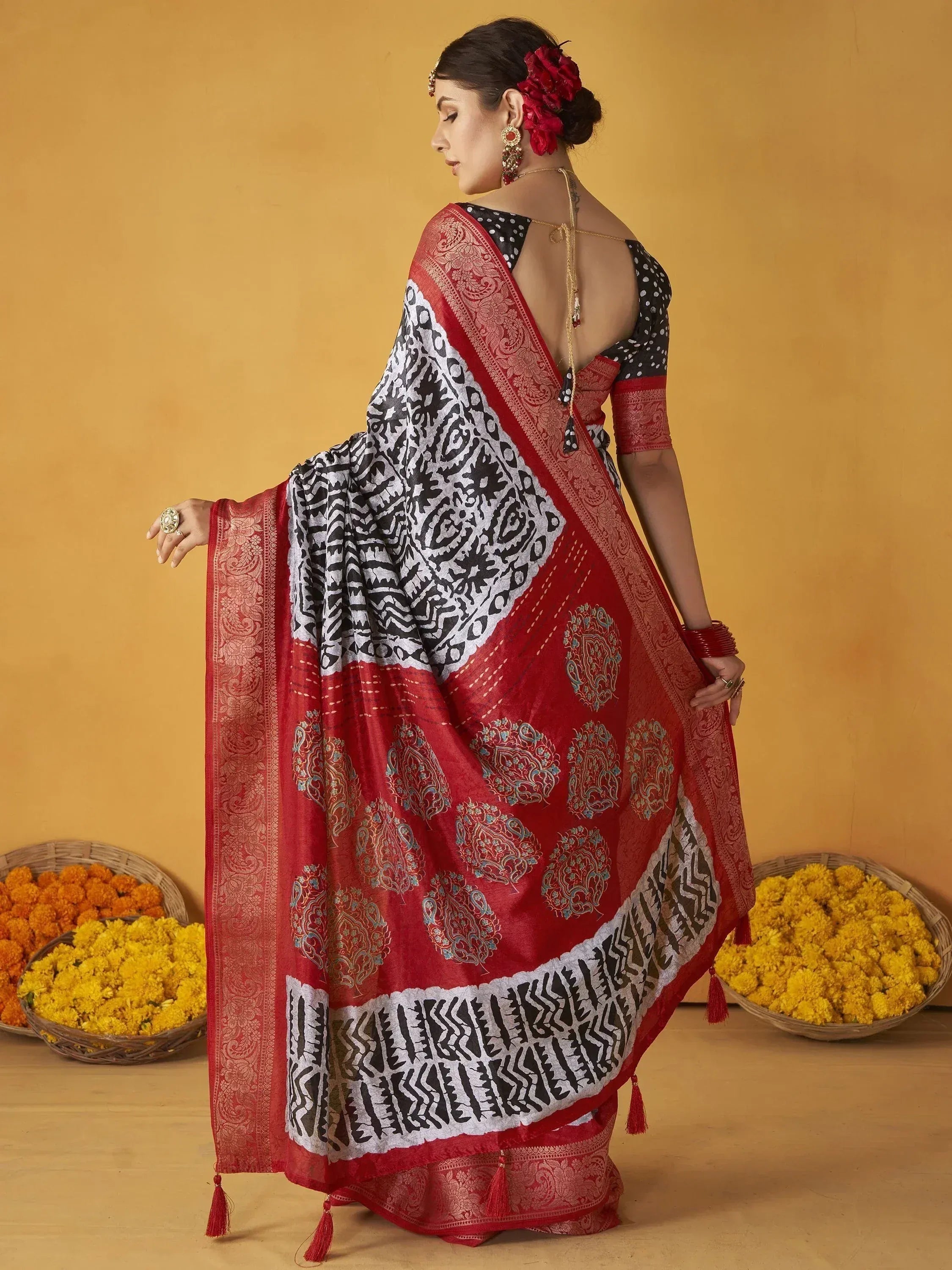 Red and black printed saree with gold paisley border, styled with polka dot blouse and floral hair accessory
