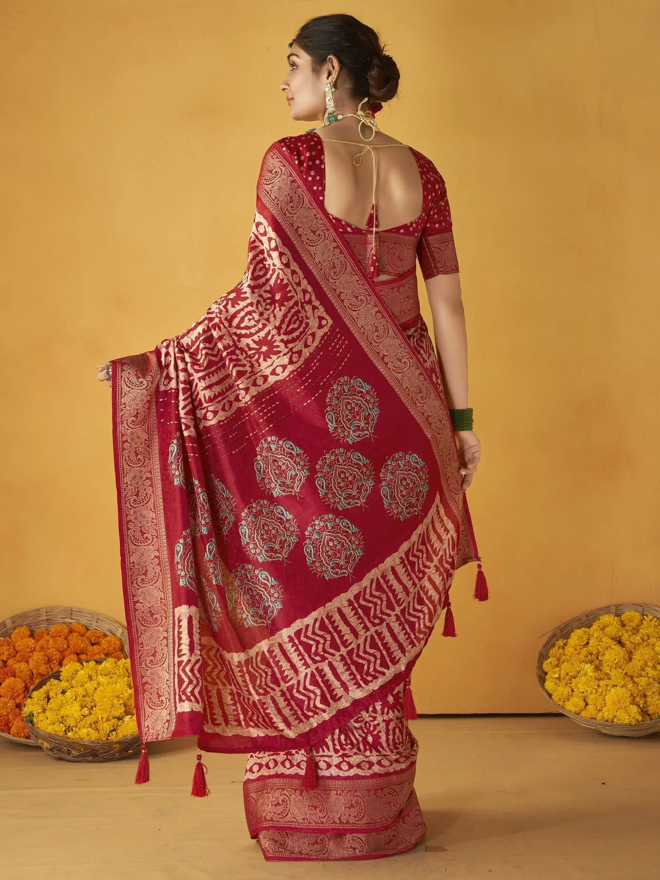 Red designer saree with gold paisley print, tassels, and backless blouse, styled with floral baskets