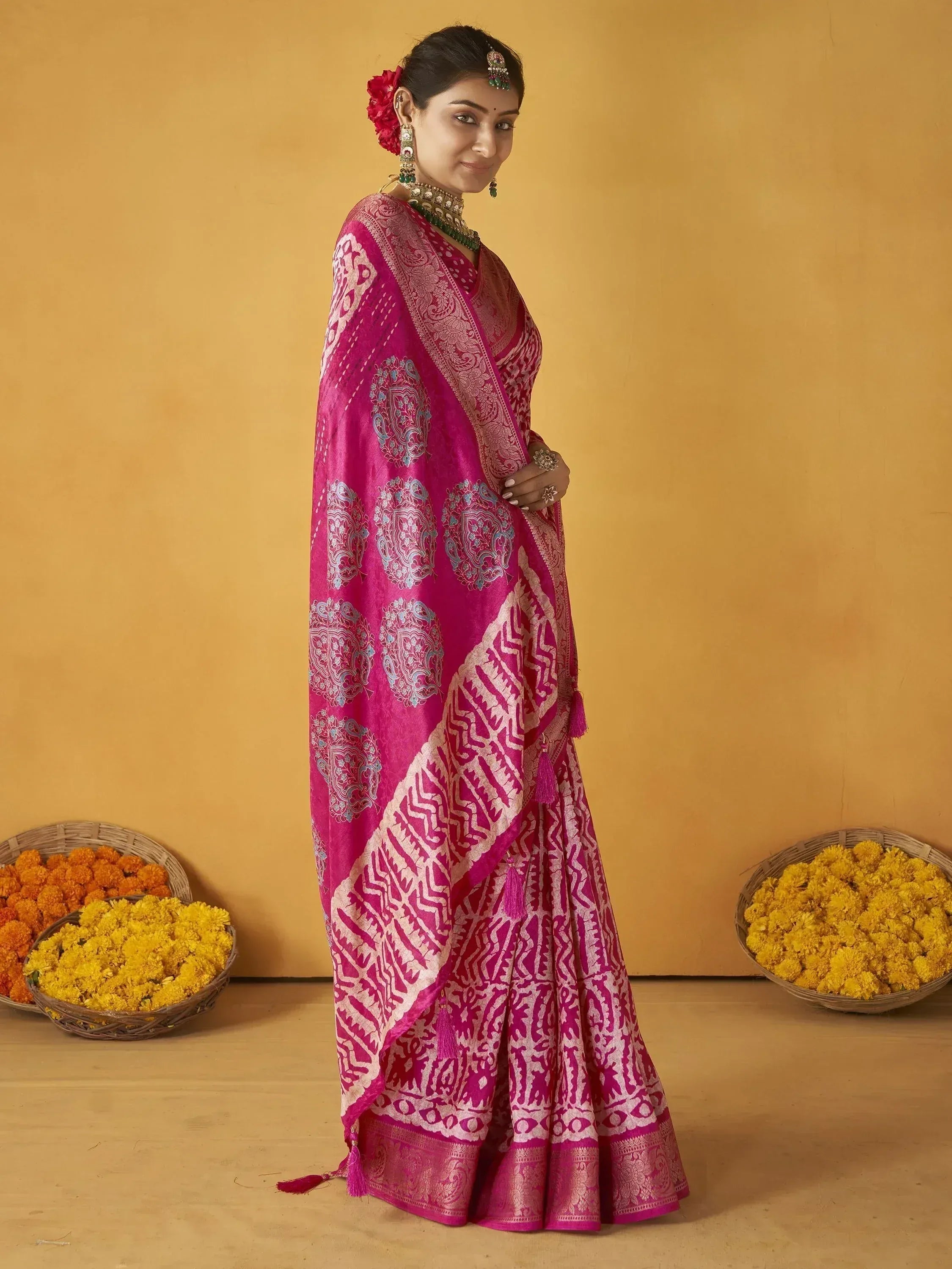 Woman in vibrant pink ethnic saree with intricate silver and blue patterns, traditional jewelry, and marigold baskets